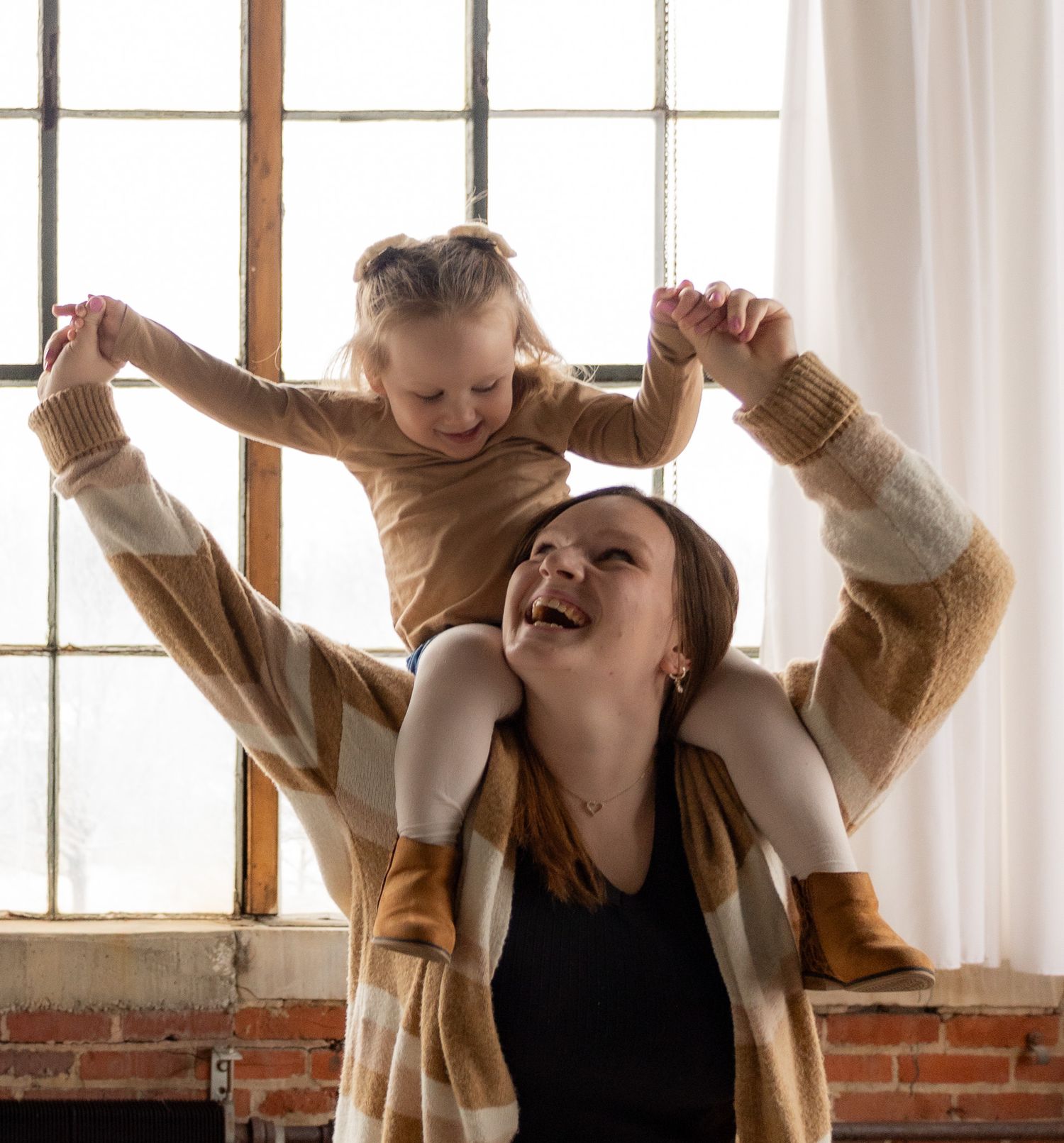 A parent and child share a joyful moment playing together near a bright window in a cozy indoor setting.