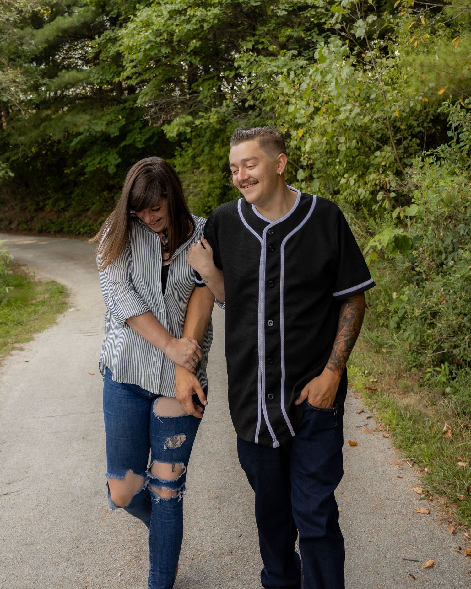Couple in casual outfits sharing laughs while walking on nature path.