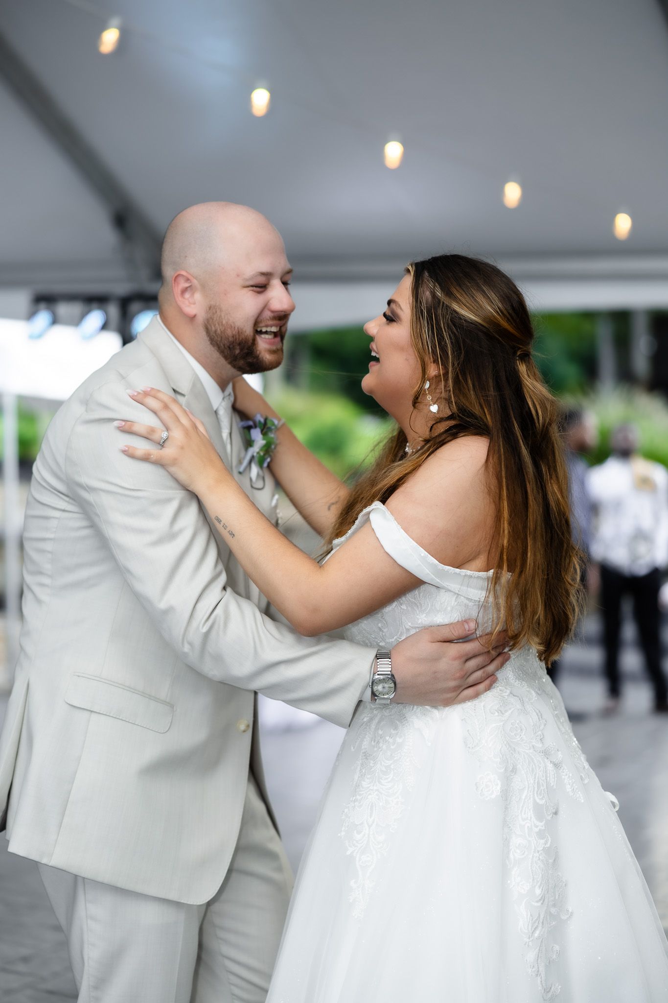 A couple shares a joyful dance moment at their wedding reception, with the bride in white and groom in light colored suit.
