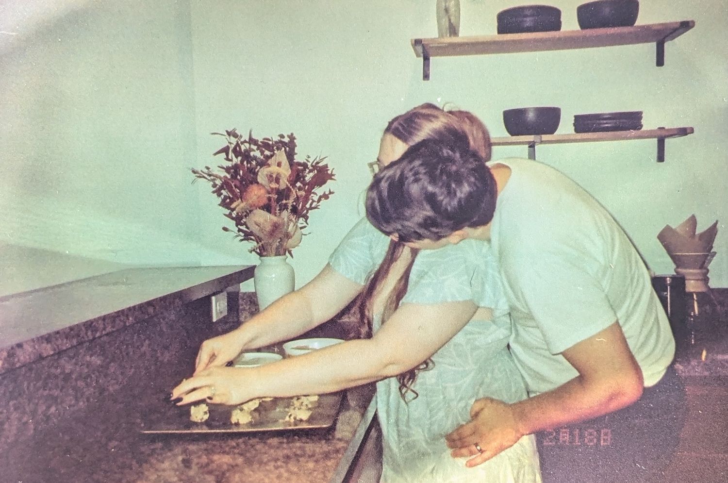 A person in a green shirt works at a vintage desk with various tools and equipment arranged on shelves.