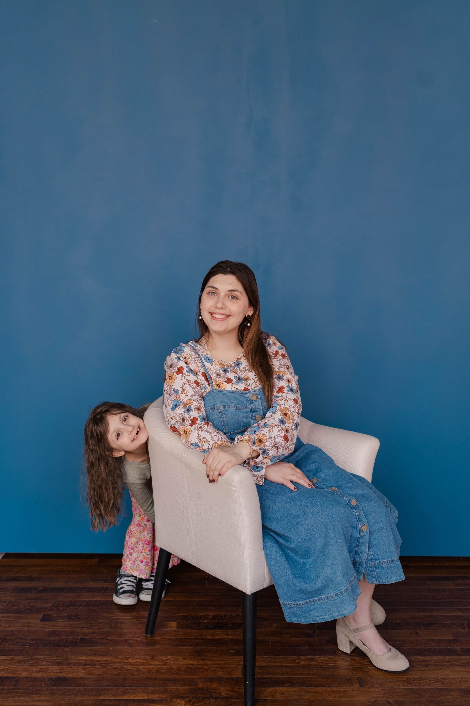 Playful portrait session against a blue wall backdrop with a comfortable grey armchair.