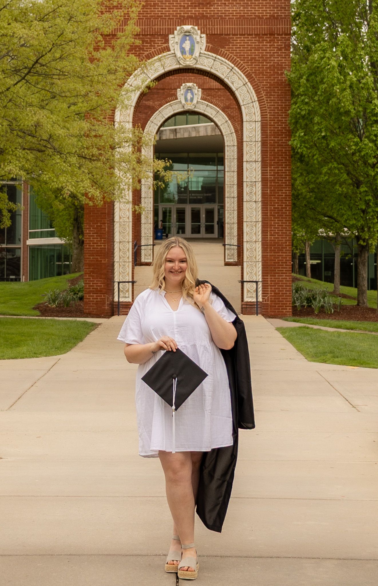 Graduate celebrates with cap in front of collegiate brick building with stone archway.