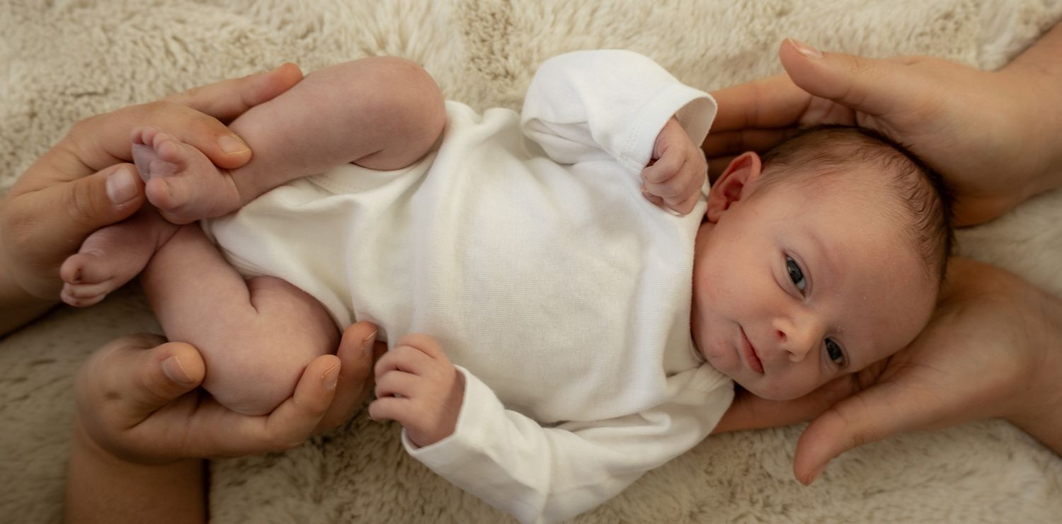 Baby in white dress lying on cream colored blanket in series of candid poses.