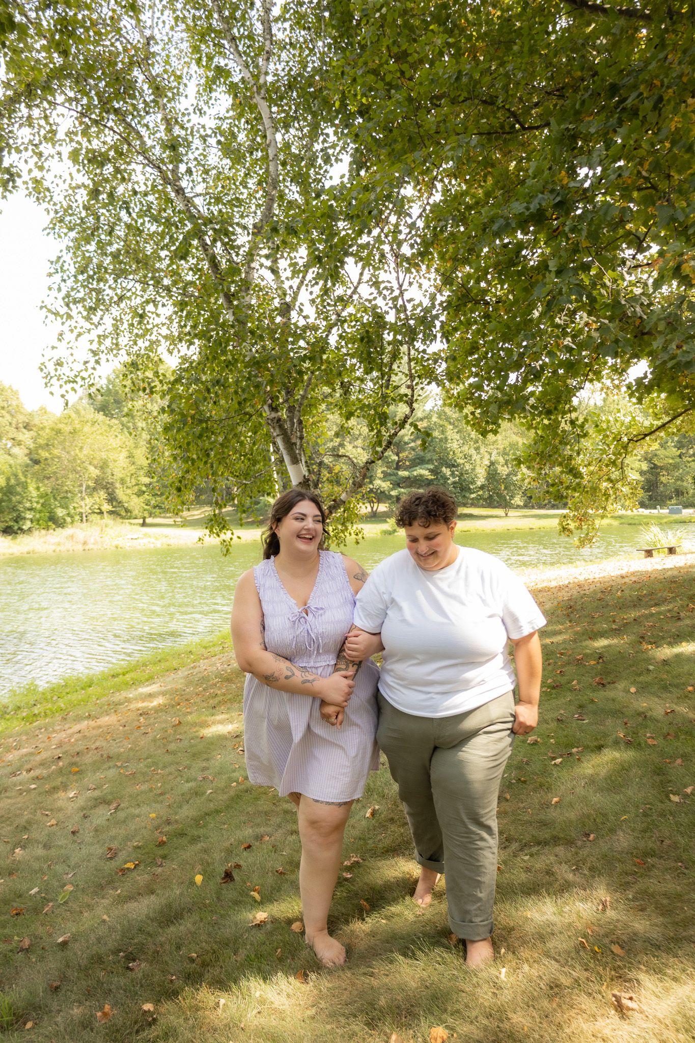 Playful couple posing together on a grassy hillside near a lake on a sunny day.