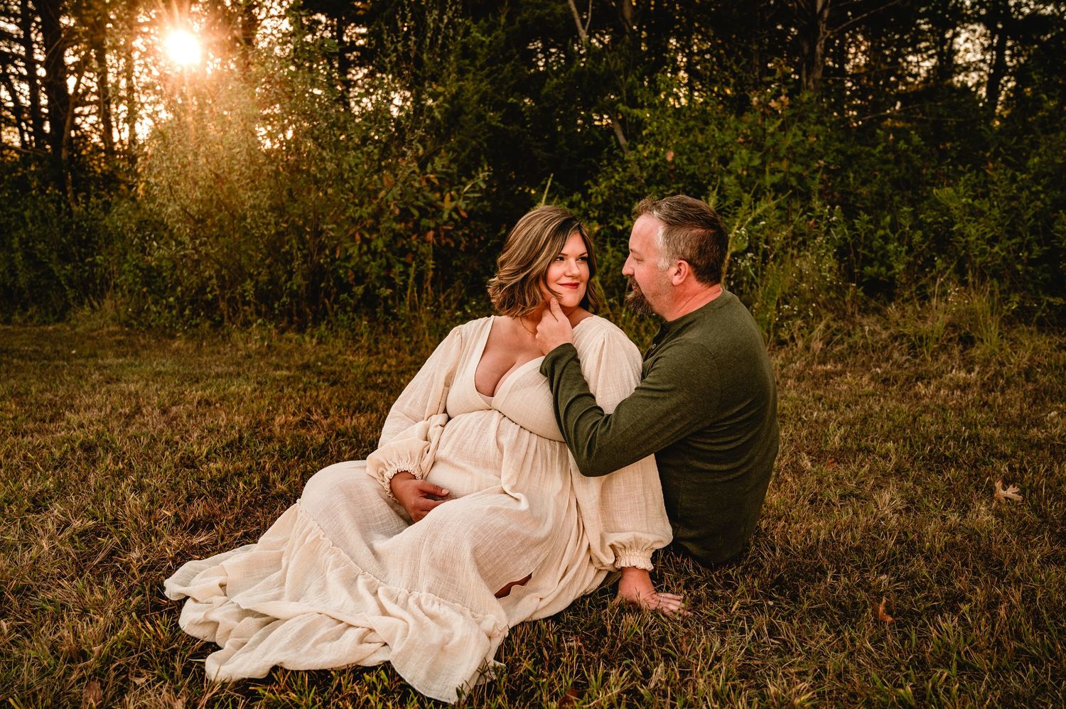 A romantic couple in wedding attire embraces during a golden sunset in a rustic outdoor setting.