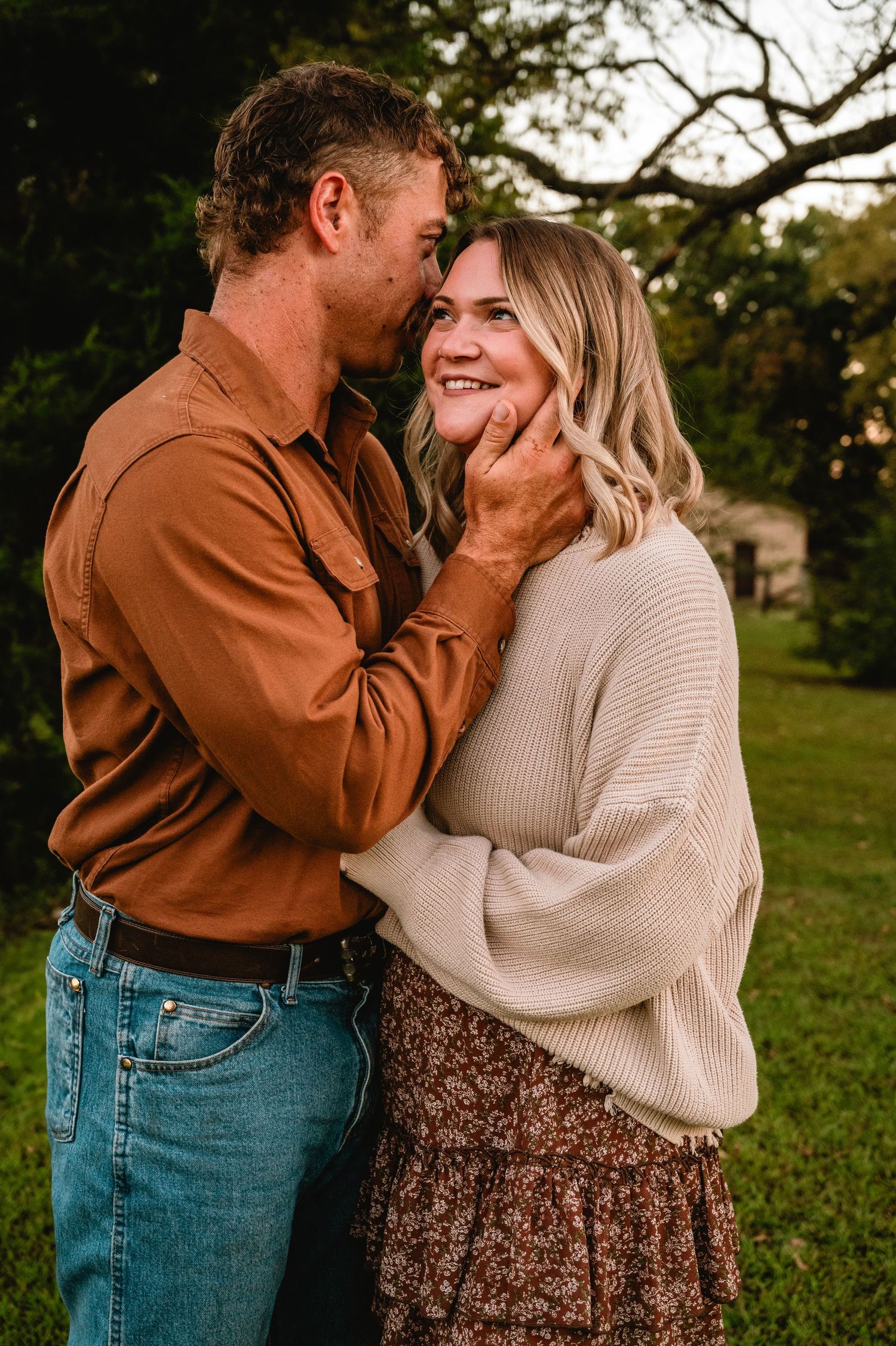 A couple shares intimate moments in a grassy outdoor setting while wearing casual fall attire.