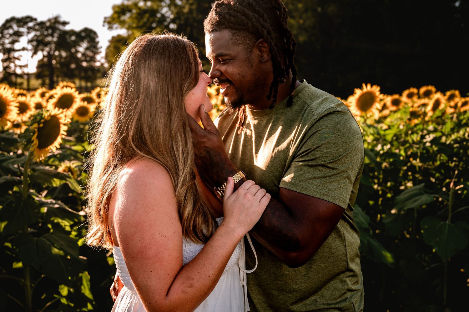 Couple sharing an intimate moment in a golden sunlit field with sunflowers in the background.