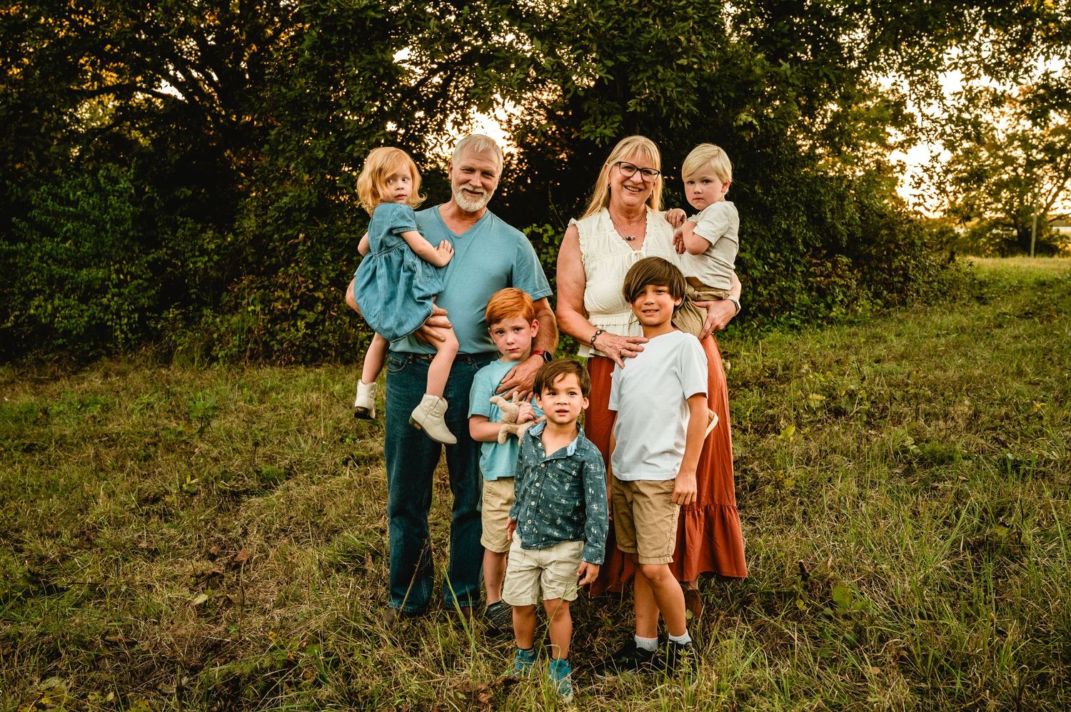 Family wearing coordinated outfits poses together in a grassy field at sunset.