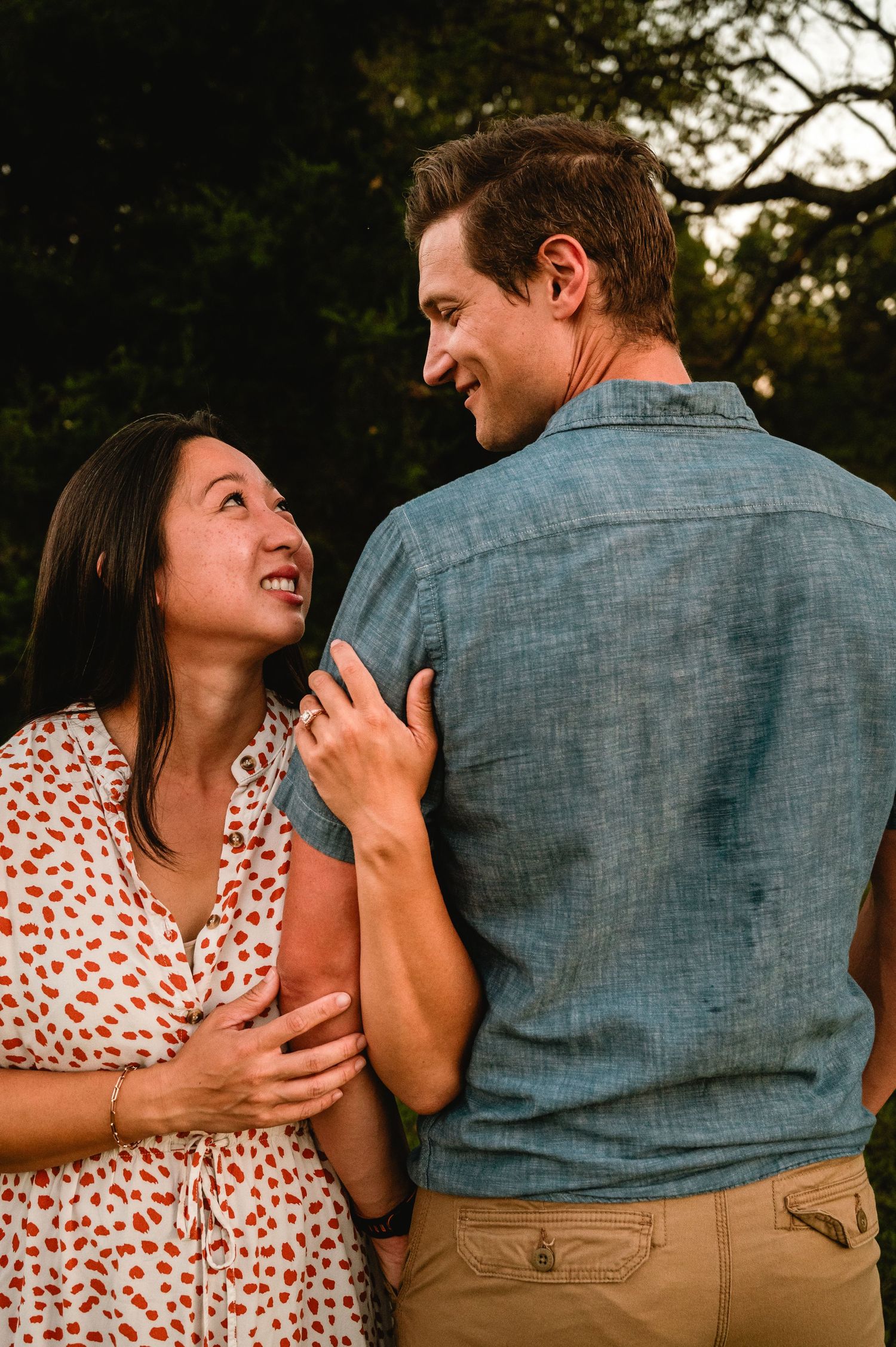 A couple in casual attire shares playful and intimate moments during a sunset photo session in a natural outdoor setting.