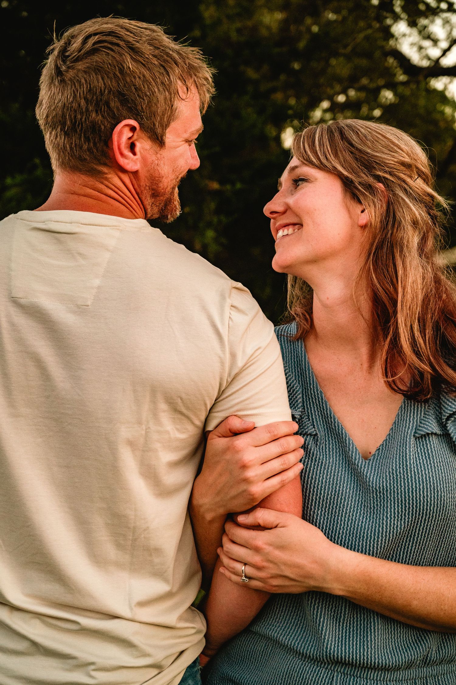 A couple shares intimate laughter and embraces in a romantic photo series against a natural outdoor setting.