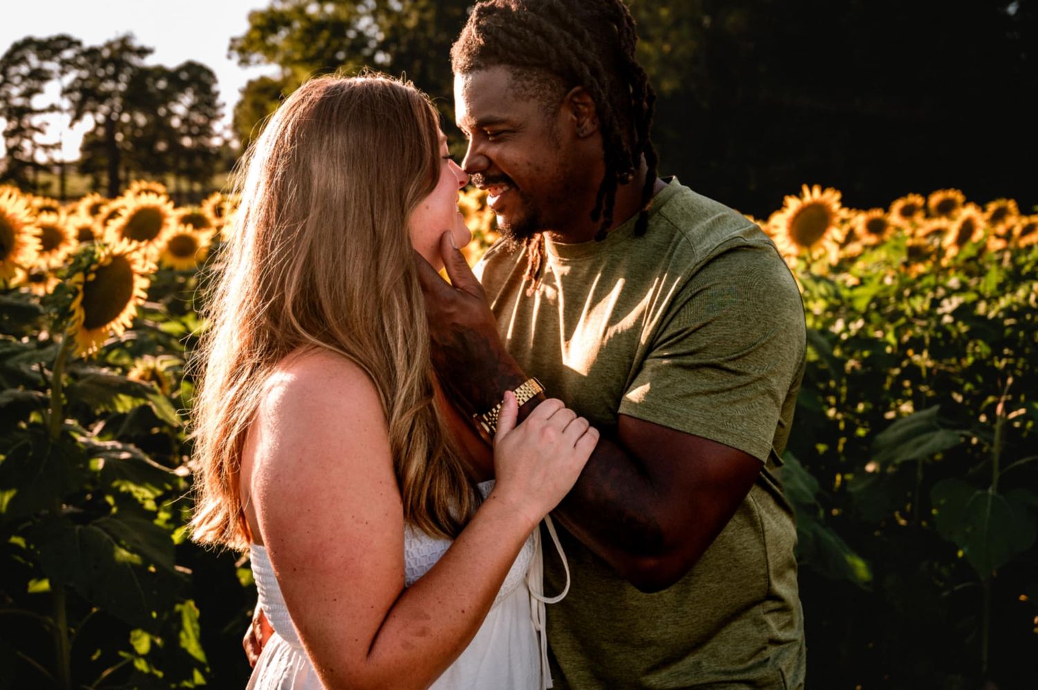 Romantic couple shares intimate moments in a sunlit sunflower field during golden hour.