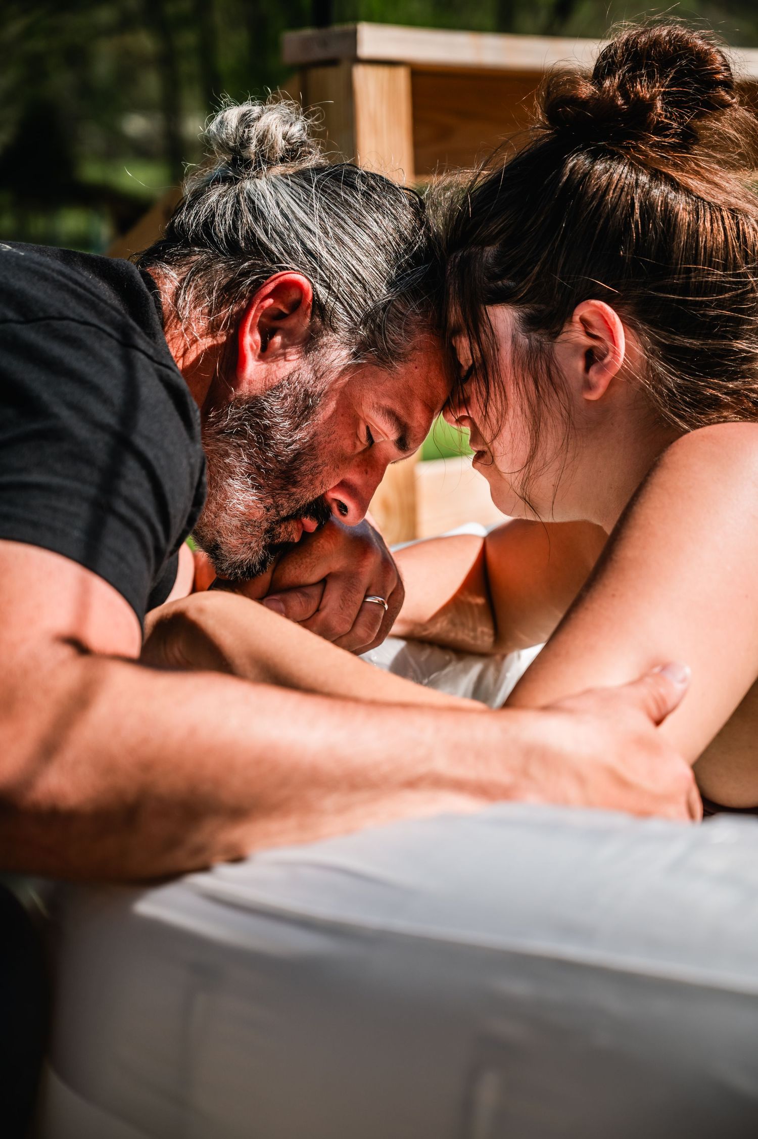 Two people with buns in their hair share an intimate moment while leaning over a white surface in warm lighting.