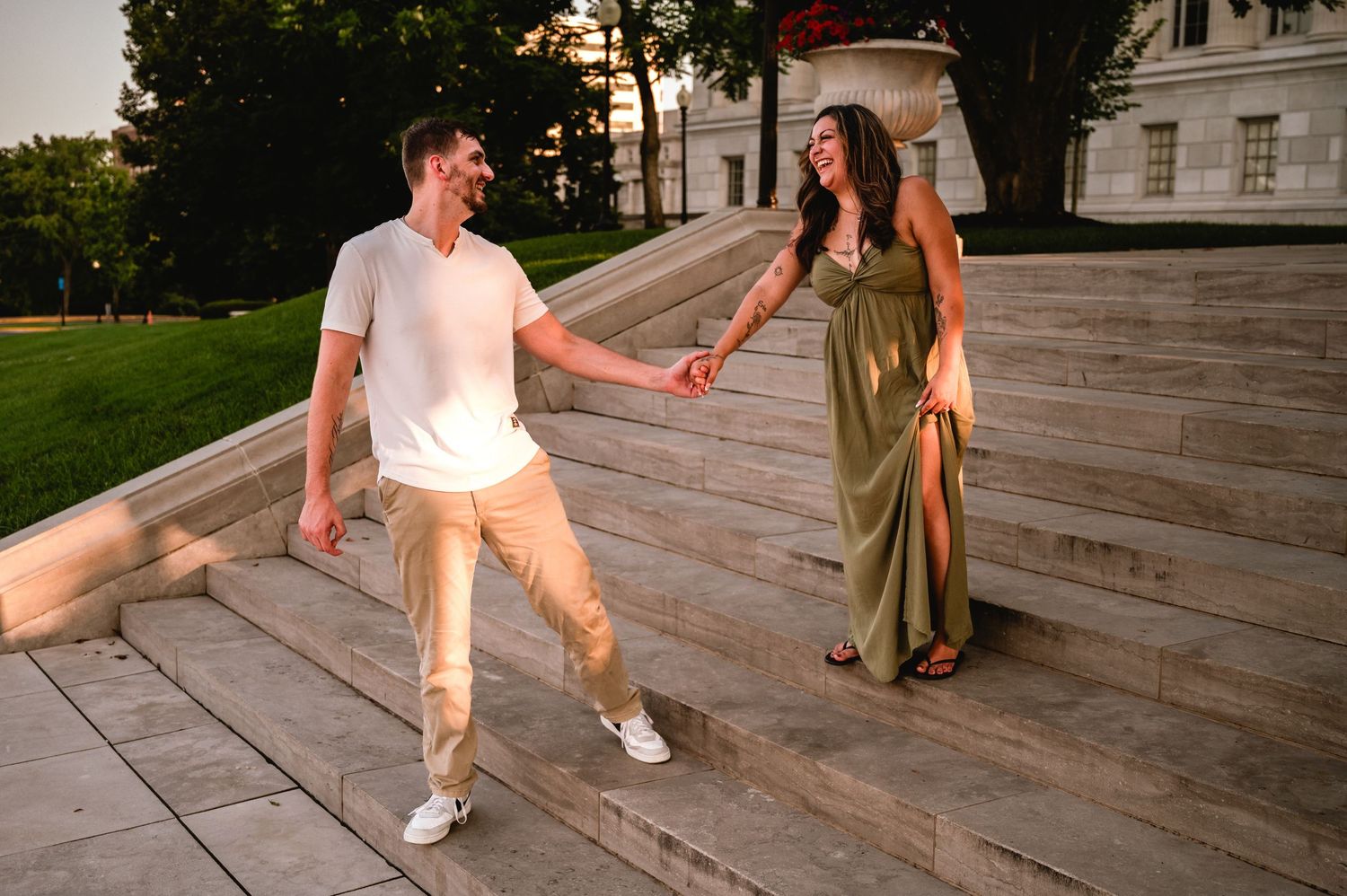 Couple holding hands on outdoor stone steps at sunset, man in white shirt and woman in green dress.
