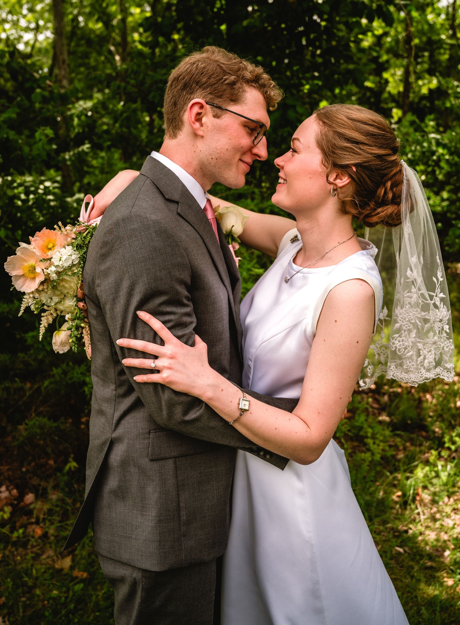 A bride and groom share a romantic moment outdoors, with the bride holding a bouquet and wearing a white dress and veil.