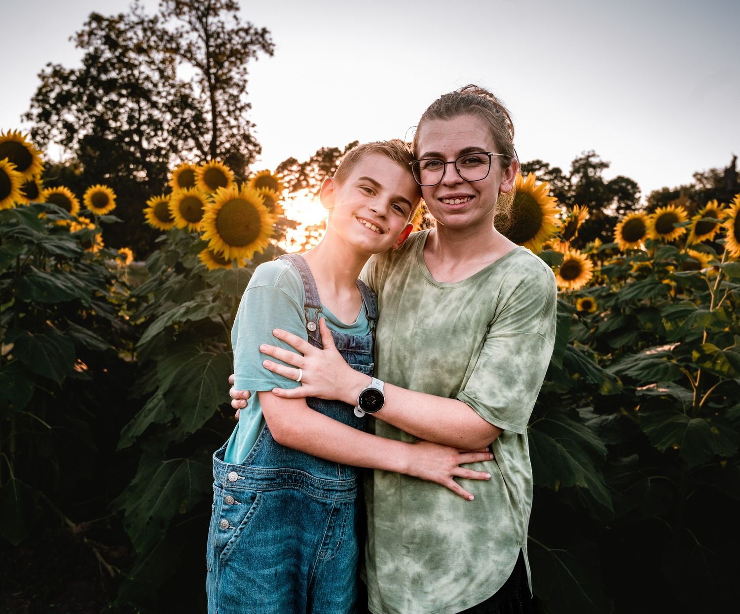 A romantic couple poses together in a vibrant sunflower field at golden hour.