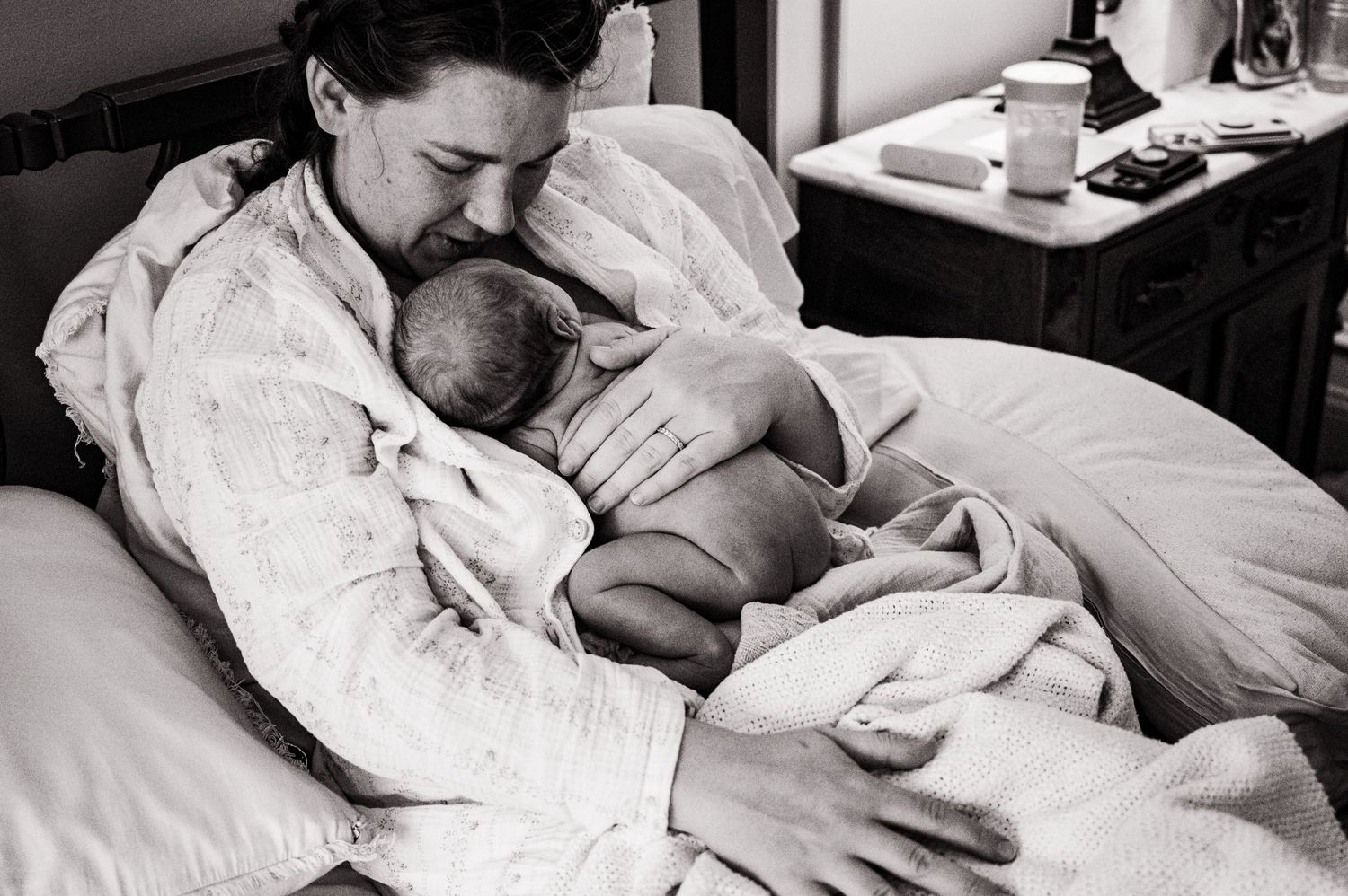 A series of black and white photos showing tender moments between a parent and newborn baby in a hospital bed.