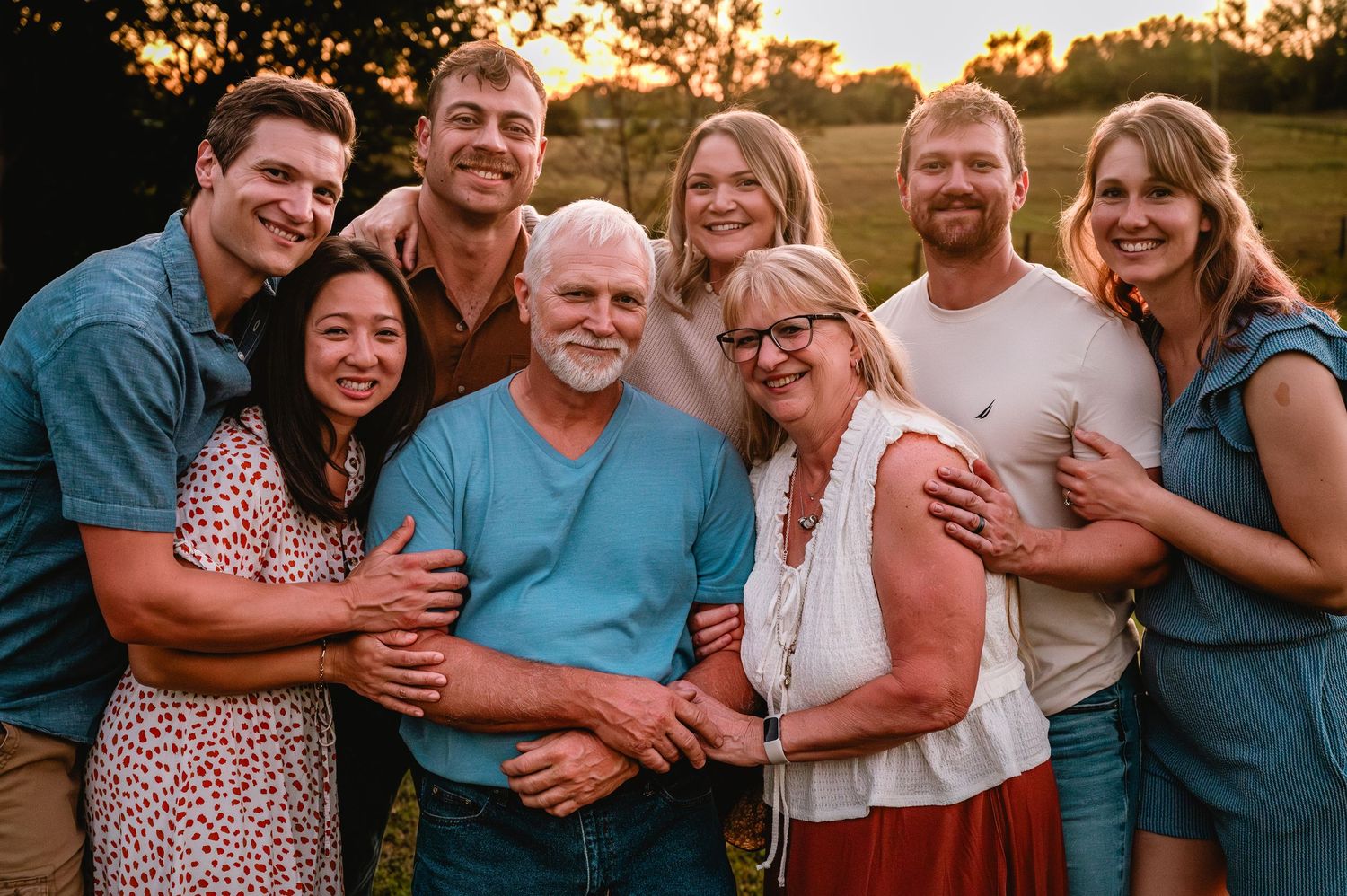 A group of people embrace and laugh together during a golden hour outdoor photo session.