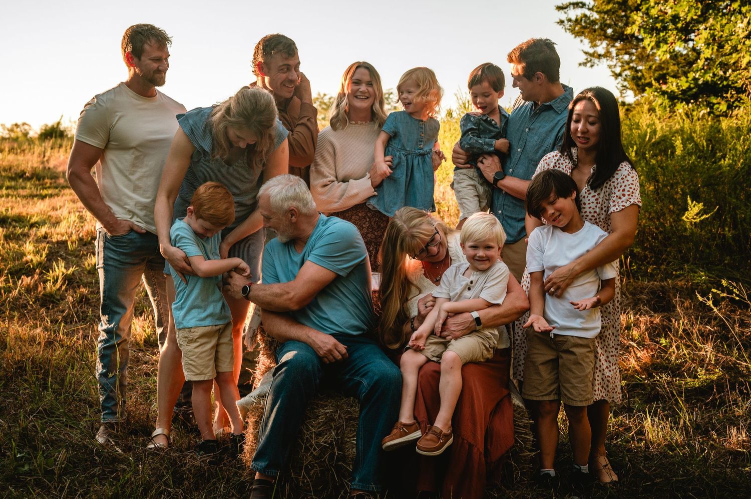 Extended family gathers outdoors during golden hour for a series of casual portrait photos in a natural setting.