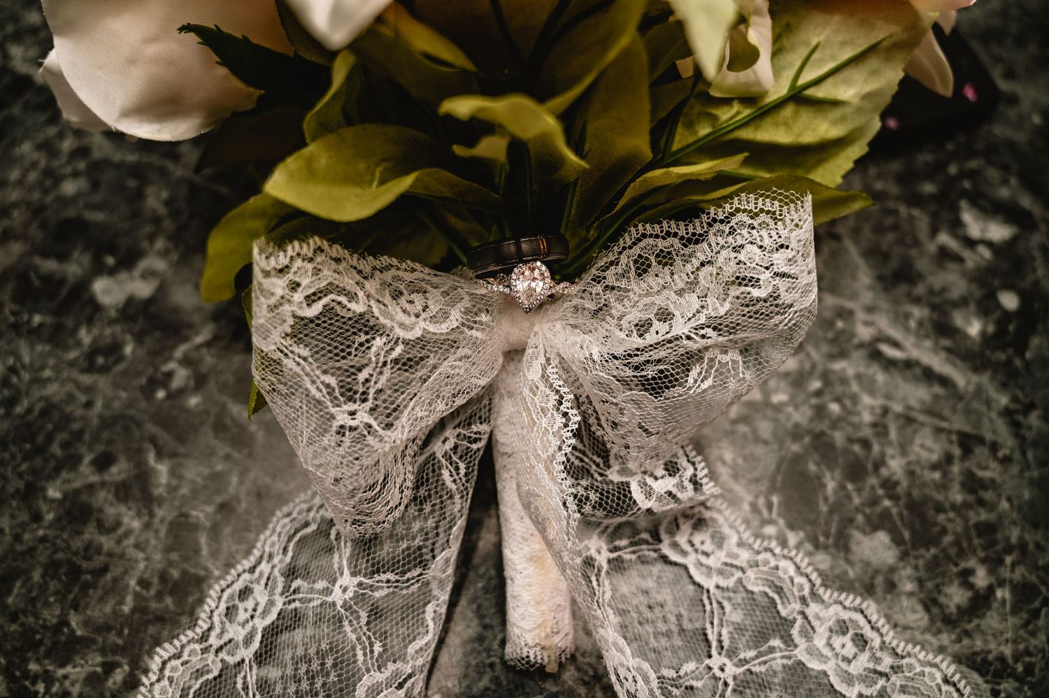 Wedding bouquet tied with delicate lace bow and vintage brooch on dark marble surface.