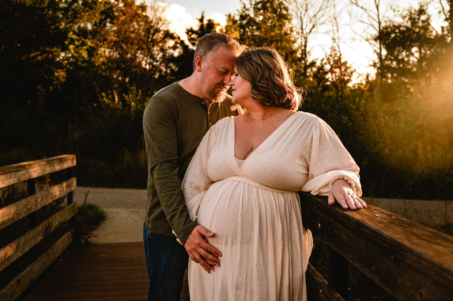 Romantic couple embraces during golden hour sunset photography session on wooden bridge walkway.