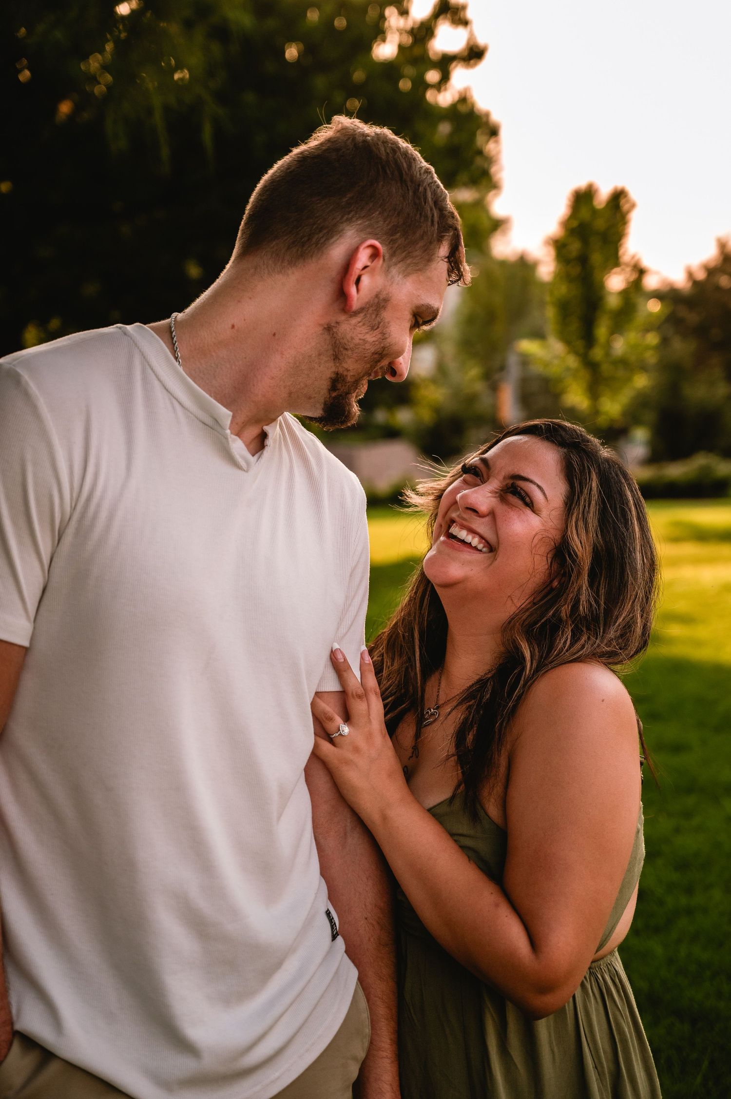 A joyful couple shares a tender moment outdoors at golden hour, with the woman laughing as they gaze at each other.