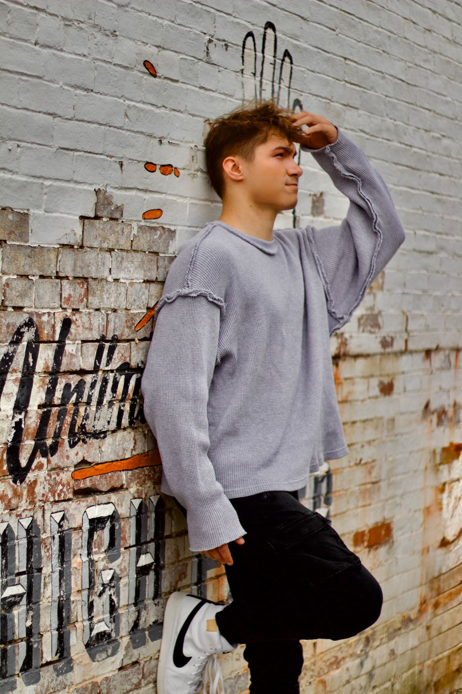 local Westfield photographer branding portrait of A person wearing a gray sweater poses against a white brick wall with graffiti.