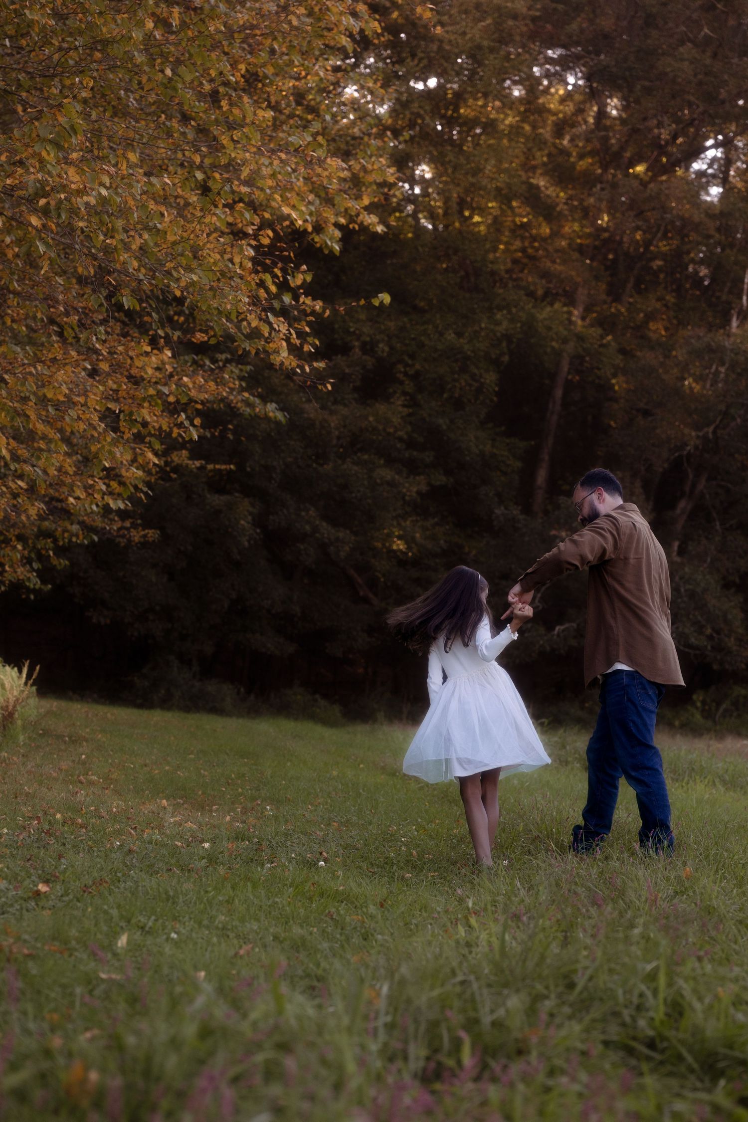 Group of people walking together on grassy hill during autumn with golden leaves on trees in background.