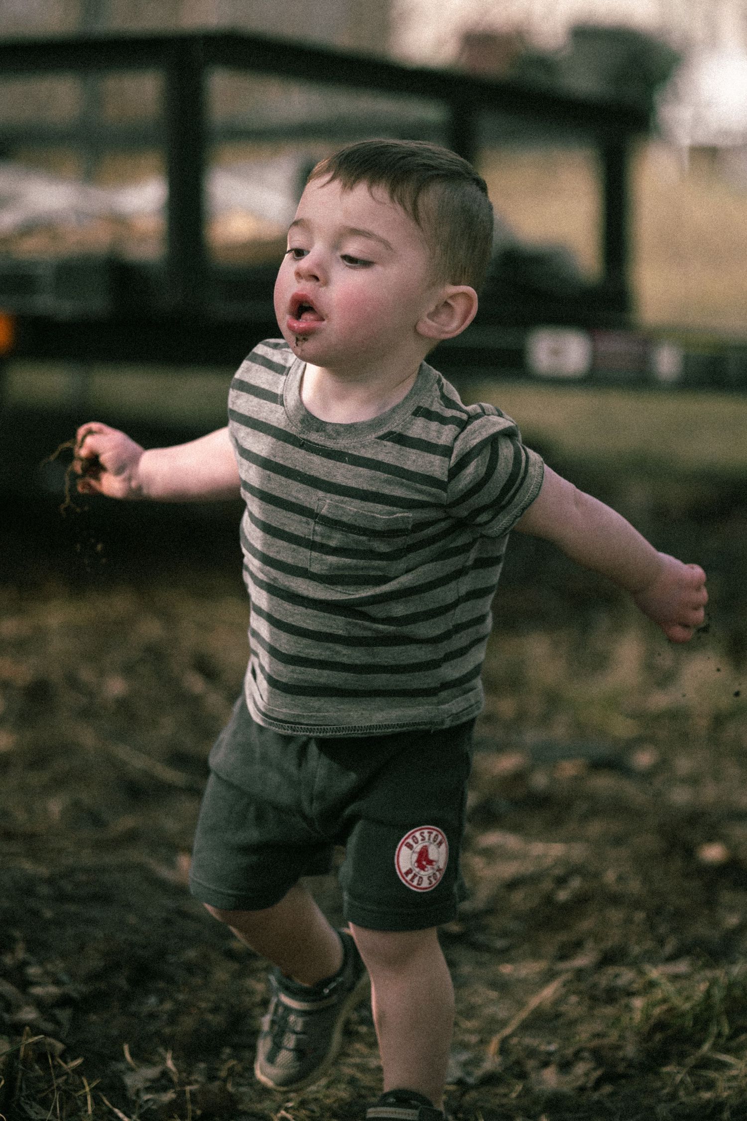 A small child in a striped shirt plays in fallen leaves on a dark autumn day.