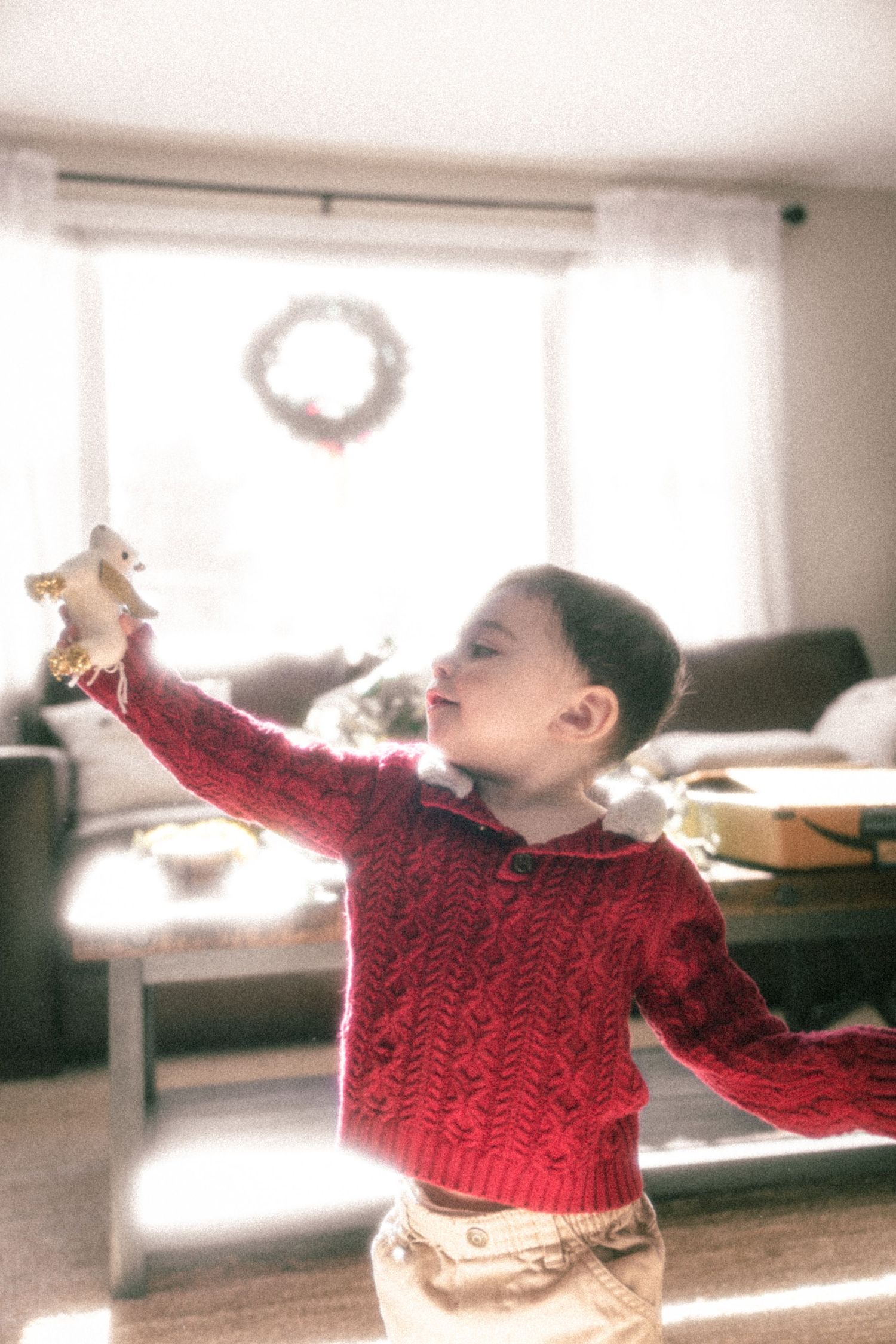 A child in a red knit sweater dances and twirls in a sunlit room.