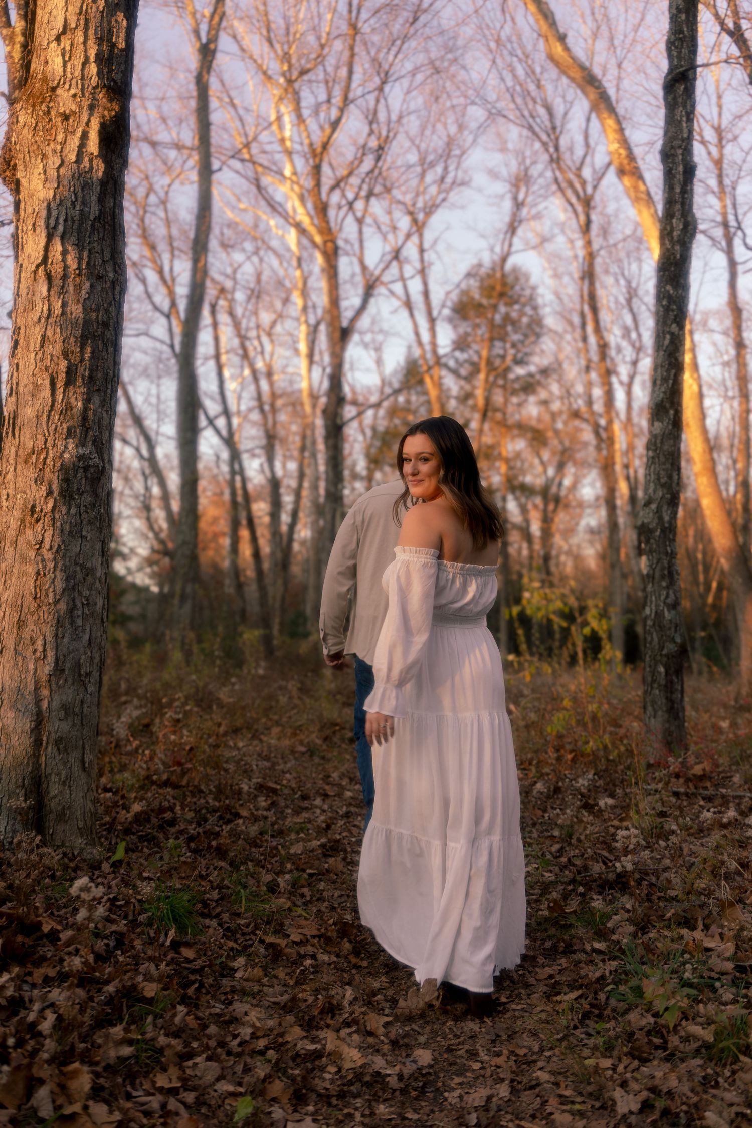 A person in a flowing white dress twirls gracefully among autumn trees during golden hour.