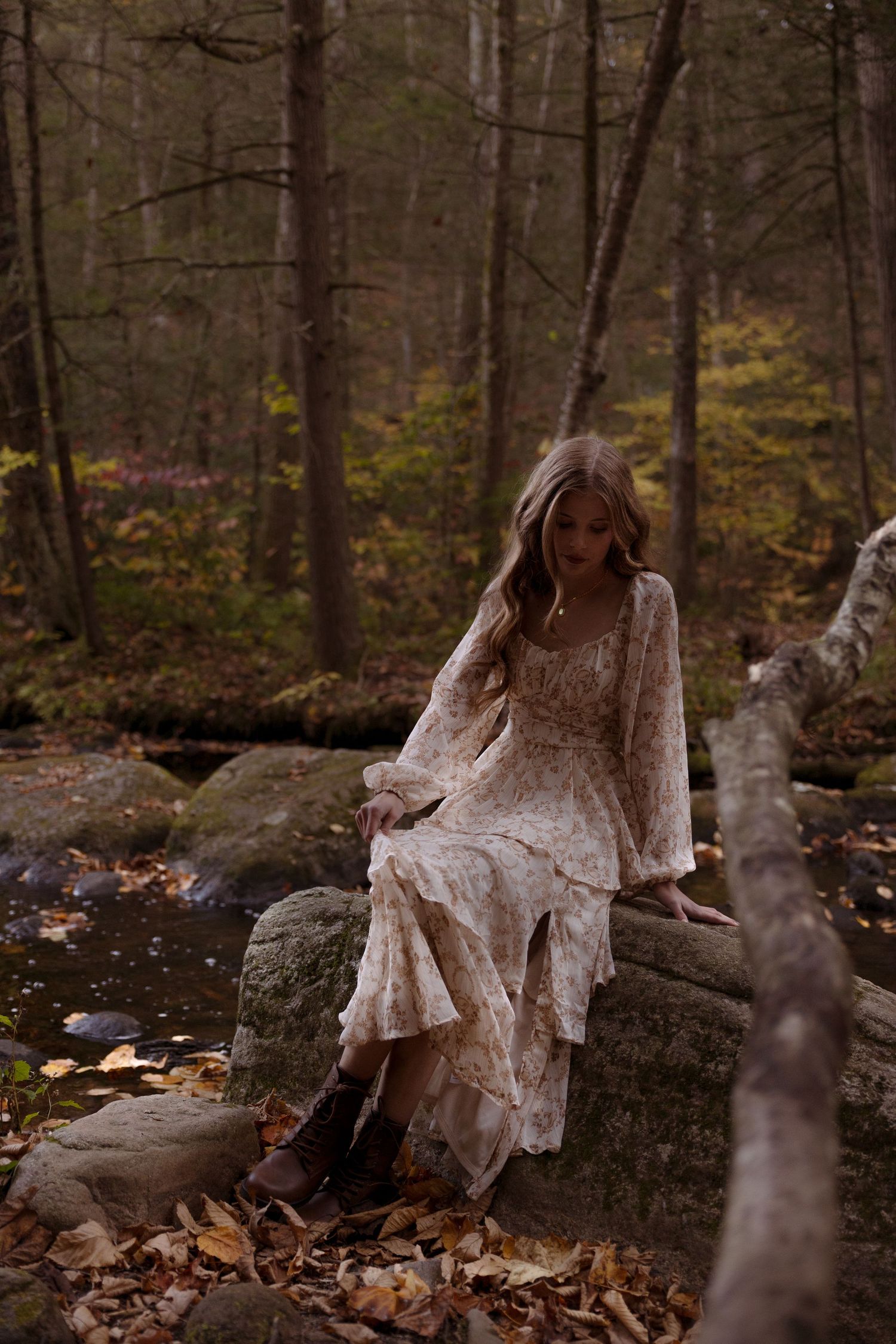A spooky figure in a white lace dress poses on mossy rocks in an autumn forest setting.