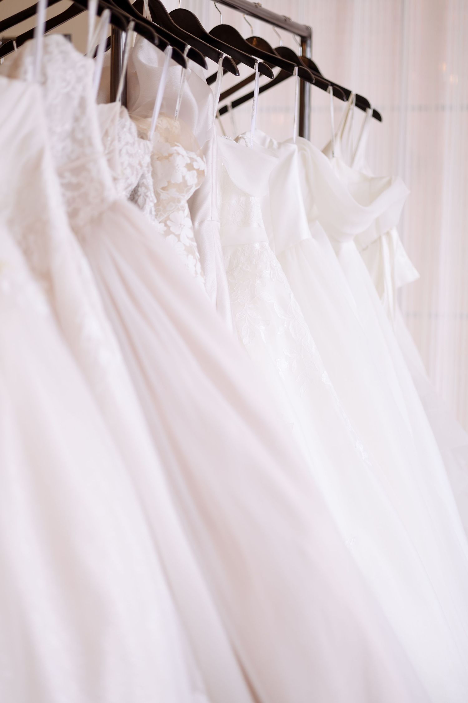 A row of elegant white wedding dresses hanging on black hangers in a bridal boutique.