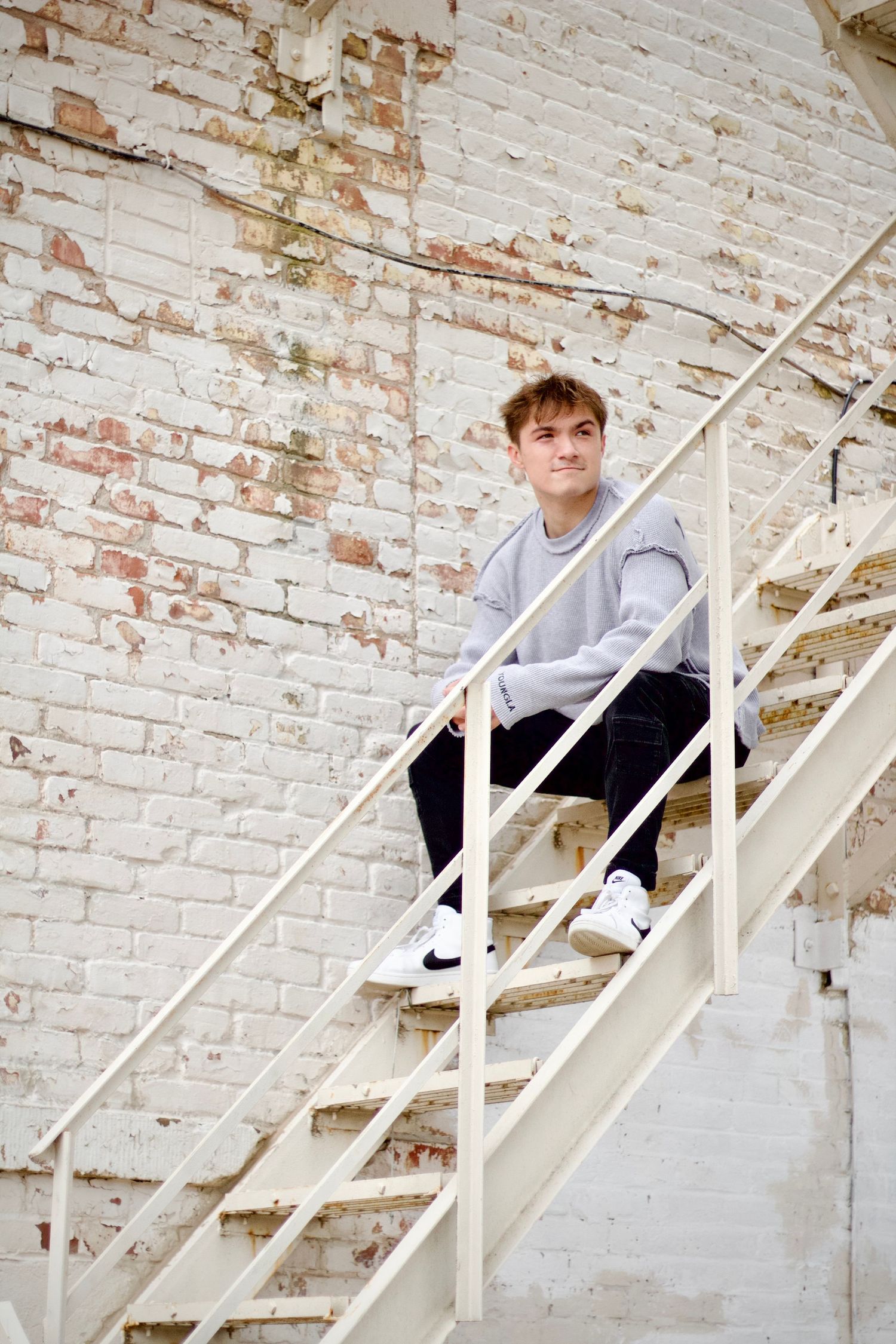 Local Westfield photographer branding portrait of A person in casual wear sits on white metal stairs against a weathered brick wall