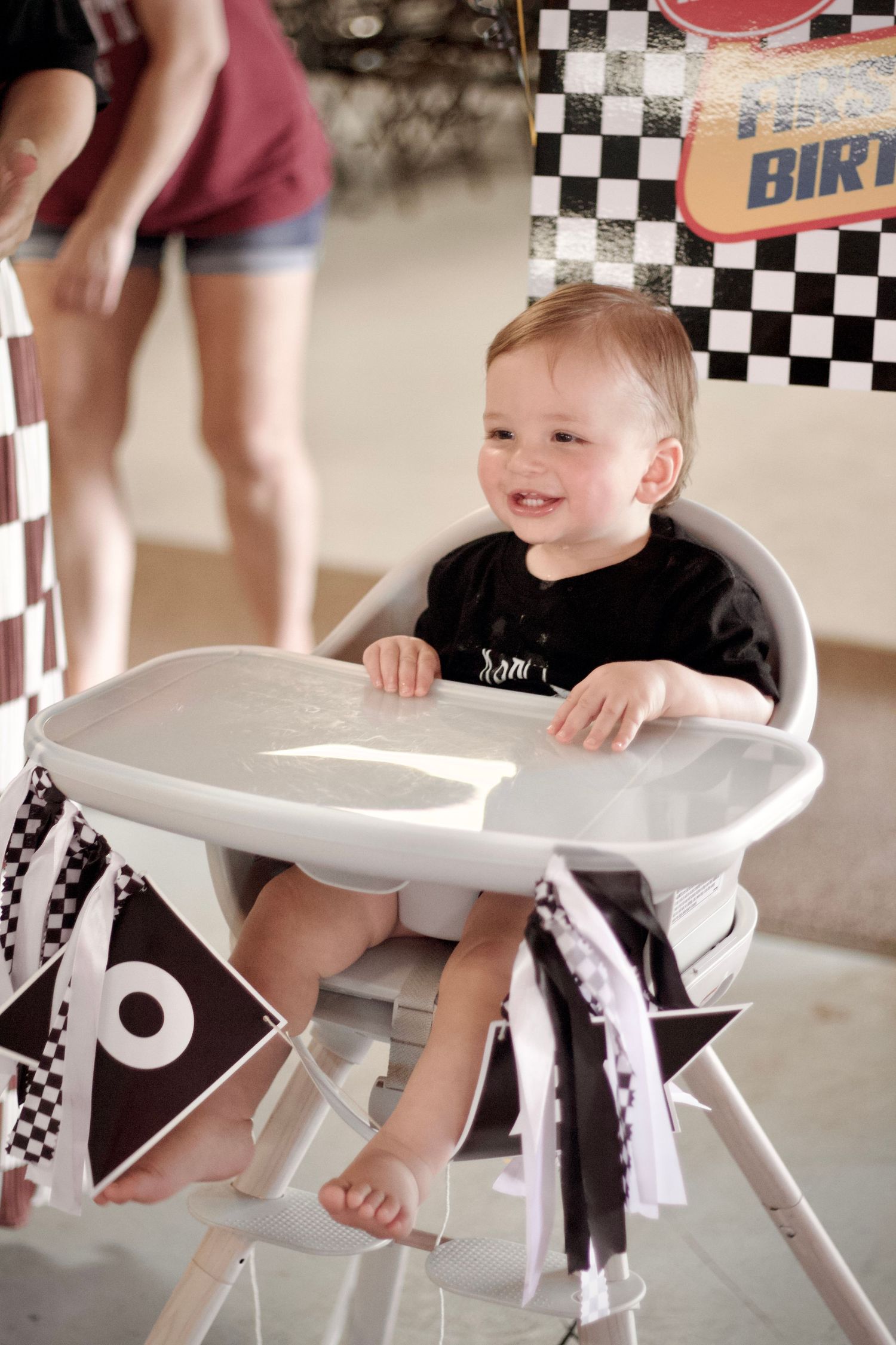 Child sits in a high chair with black and white checkered racing theme decor around the seating area.