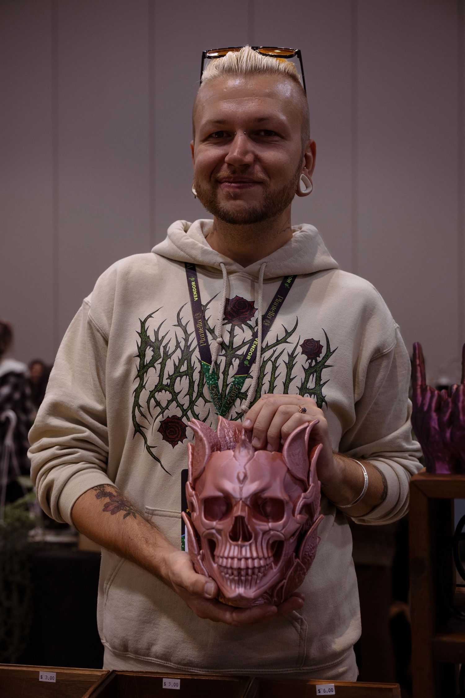 A person in a beige hoodie holds a decorative pink skull with intricate green detailing across multiple photos.