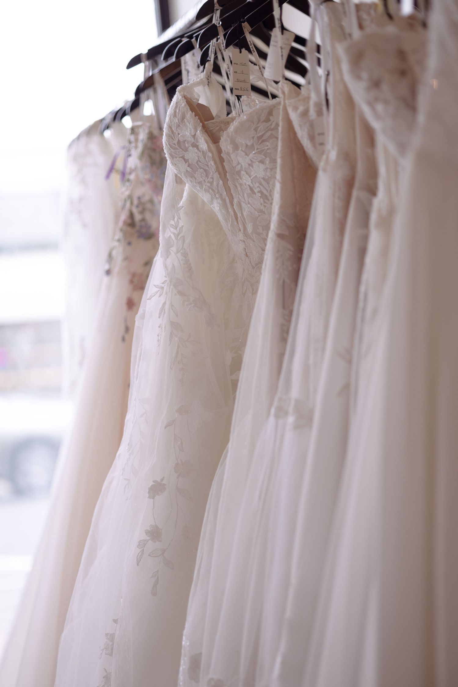 Row of elegant white and ivory wedding gowns with lace details hanging on hangers in a bridal boutique.