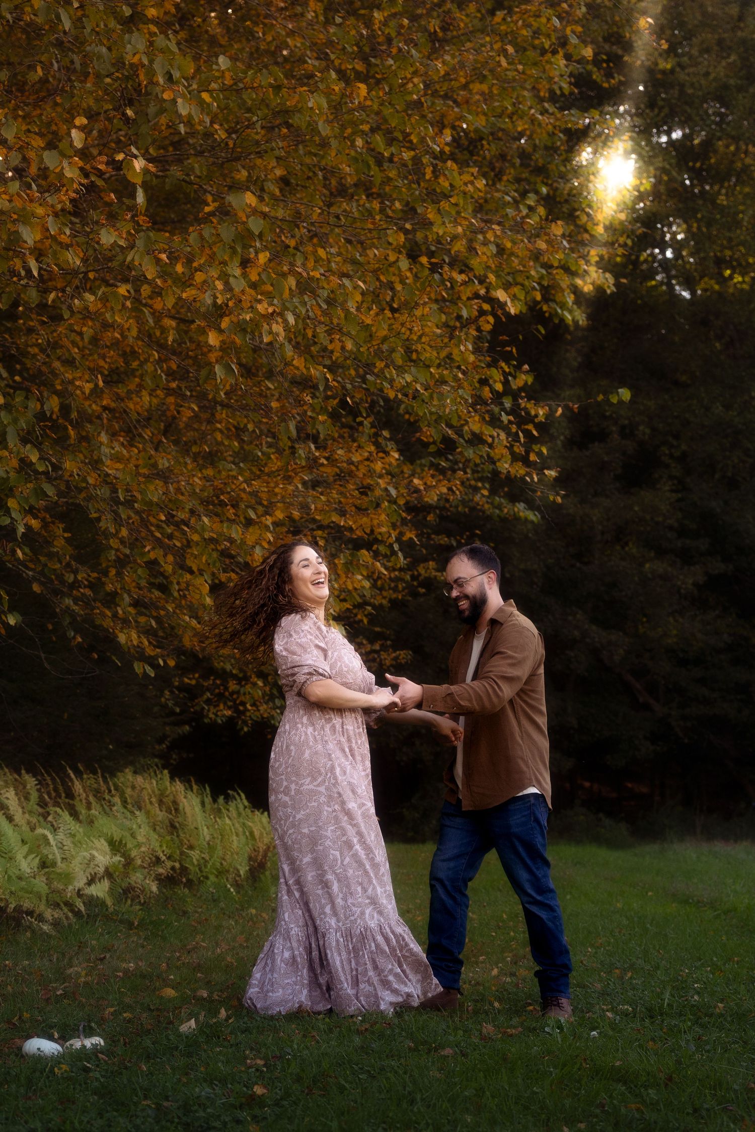A couple dances together in an autumn park setting with golden leaves and sunlight filtering through the trees.
