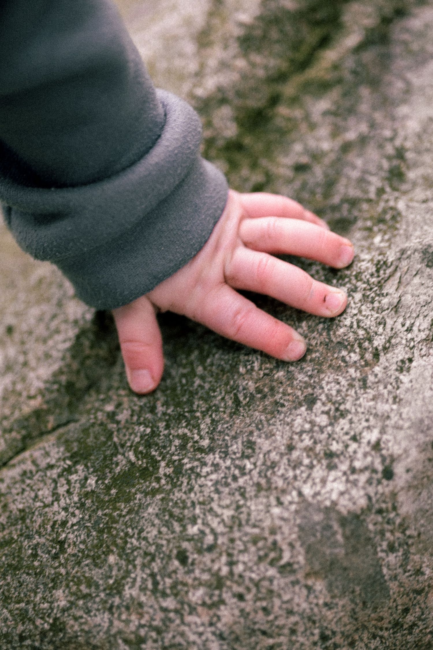 A hand in a dark sleeve touches a textured stone or concrete surface.