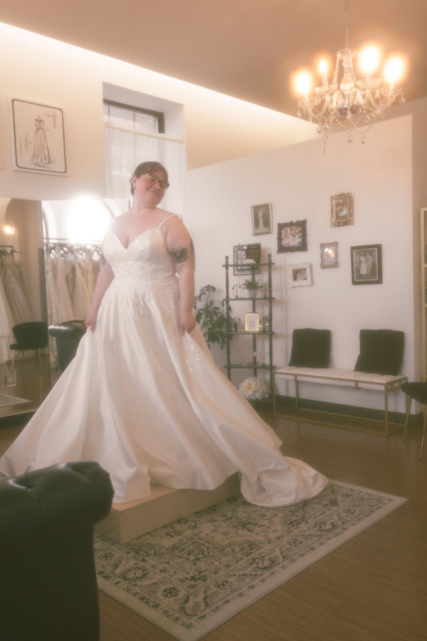 Bride in a flowing white ball gown with lace bodice and spaghetti straps poses in an elegant bridal boutique.
