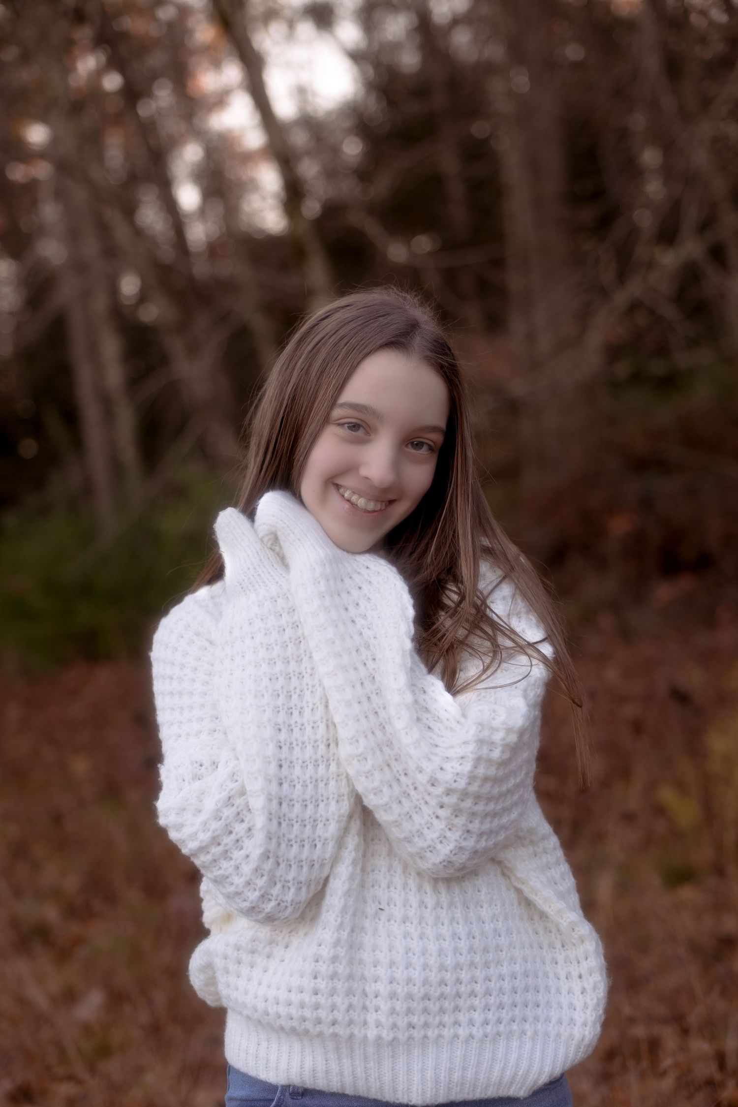 A person wearing a cozy white knit sweater poses outdoors against an autumn forest background.