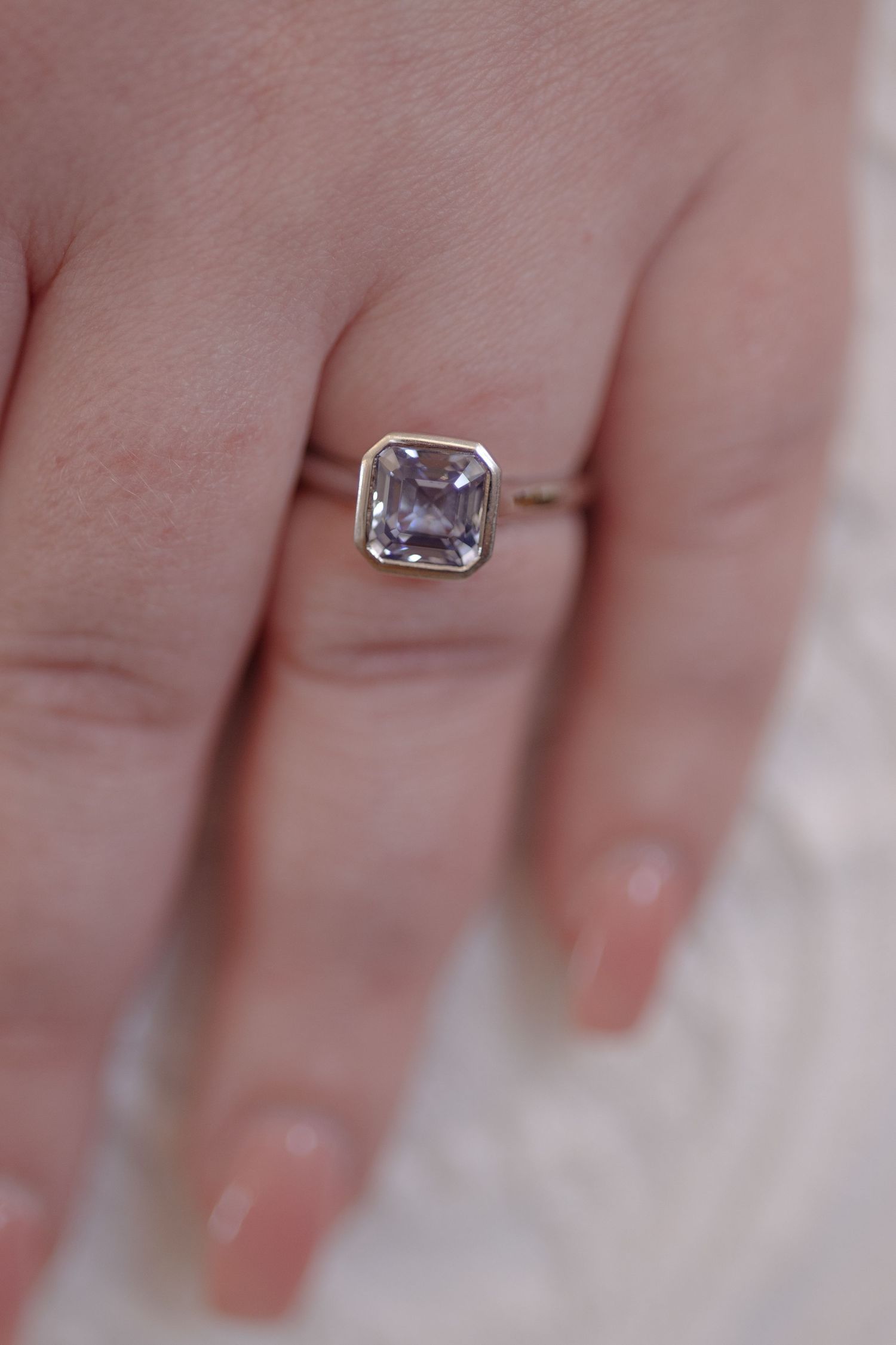 Hand wearing a bezel-set cushion cut lavender gemstone solitaire ring on a delicate gold band.