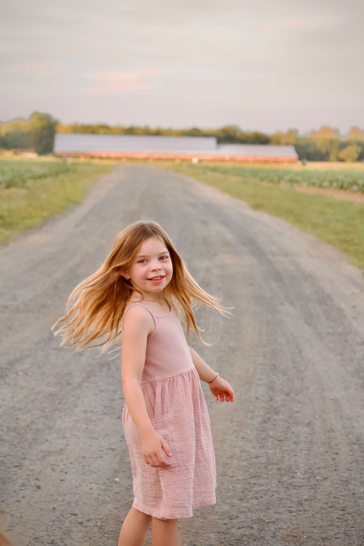 Local Westfield family photographer photo of a child in a pink dress running and playing on a rural dirt road during golden hour.