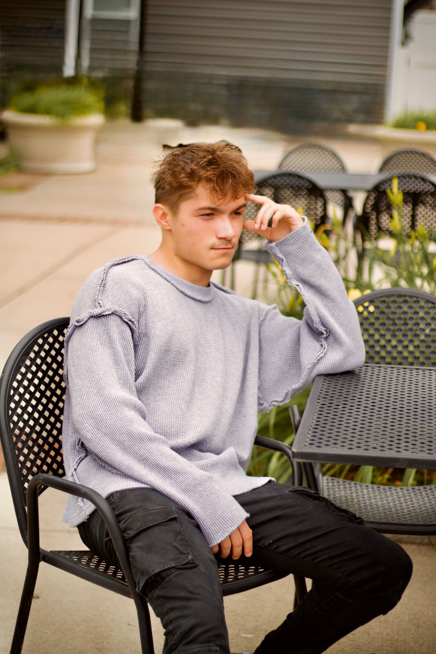 Local westfield photographer branding portrait of A person wearing a gray sweatshirt lounges in black patio furniture outdoors.
