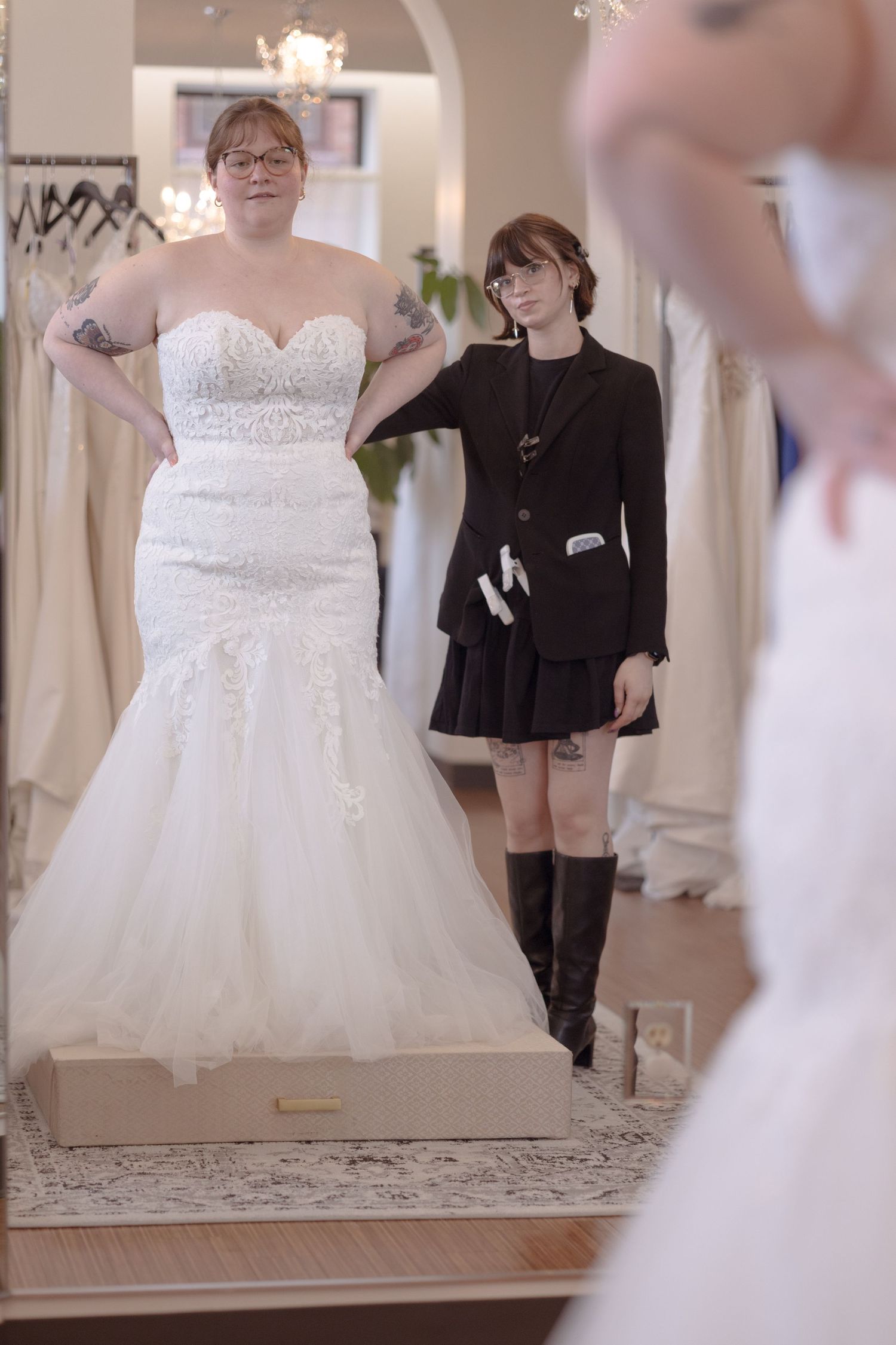 Bride trying on a white mermaid wedding dress in a bridal boutique with a stylist assisting her.