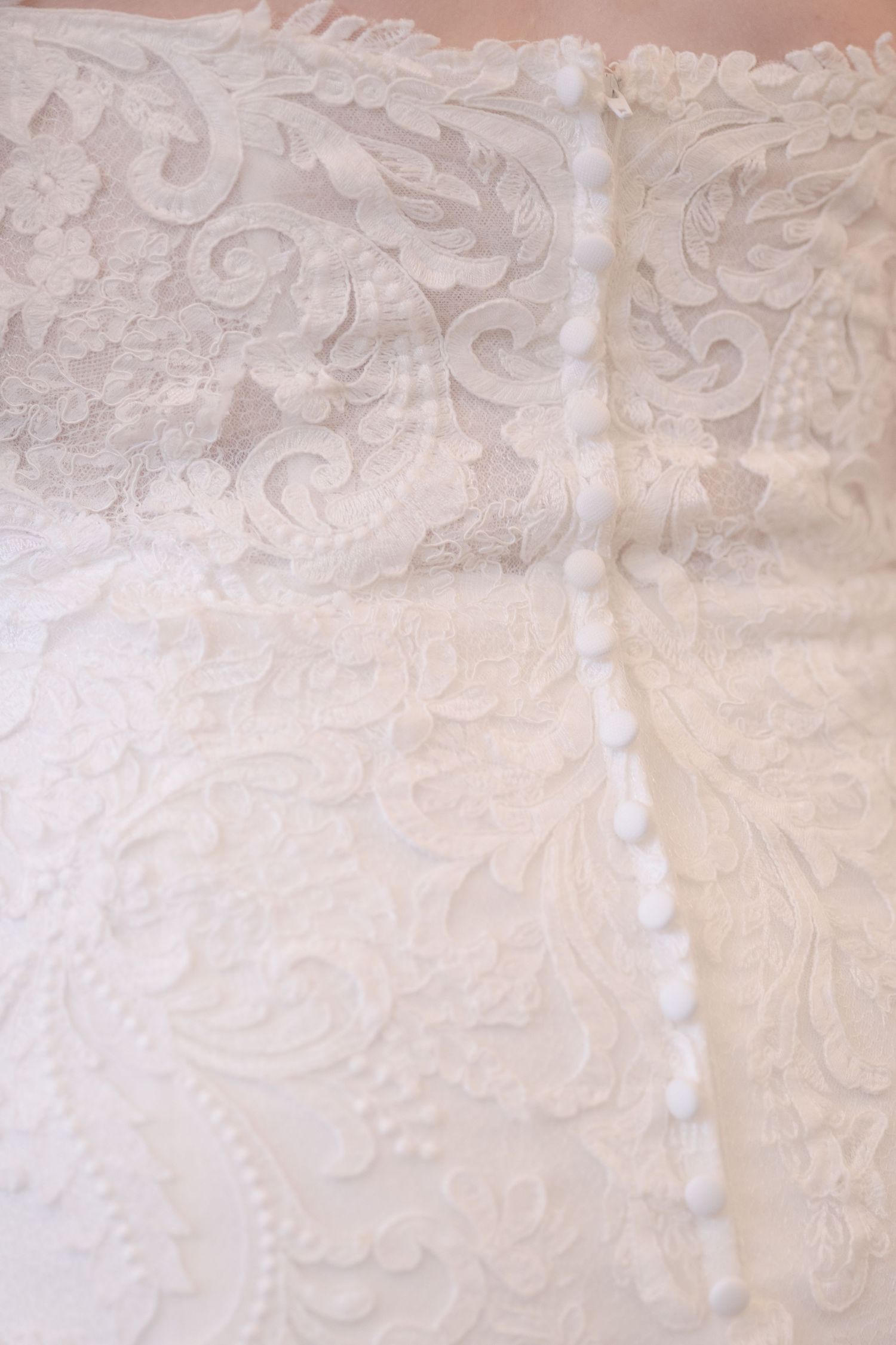 Close-up of elegant white lace fabric with intricate floral and scroll embroidery patterns on a wedding dress.