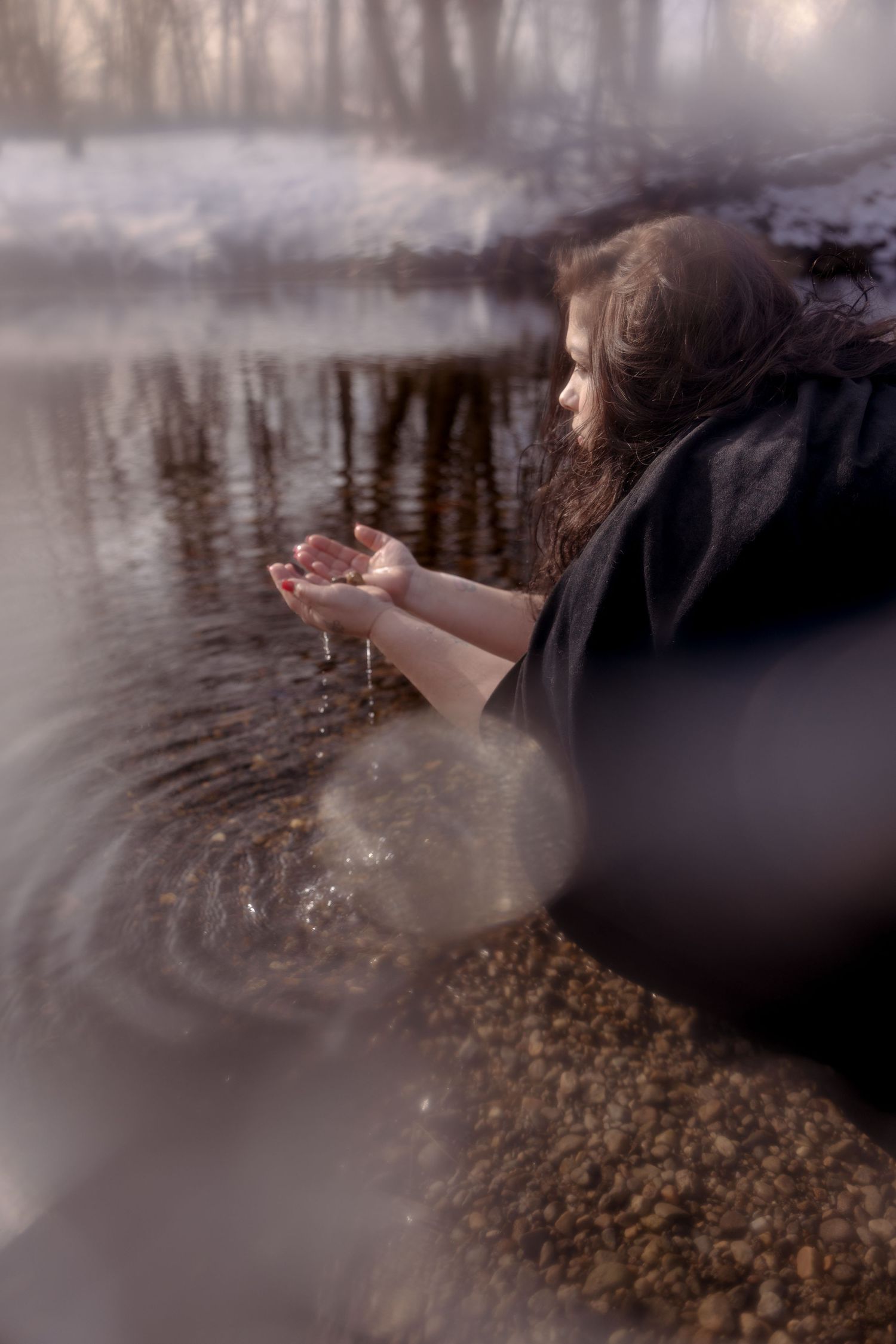 Person in dark clothing releases glowing fairy lights over reflective water surface at dusk creating magical atmosphere.