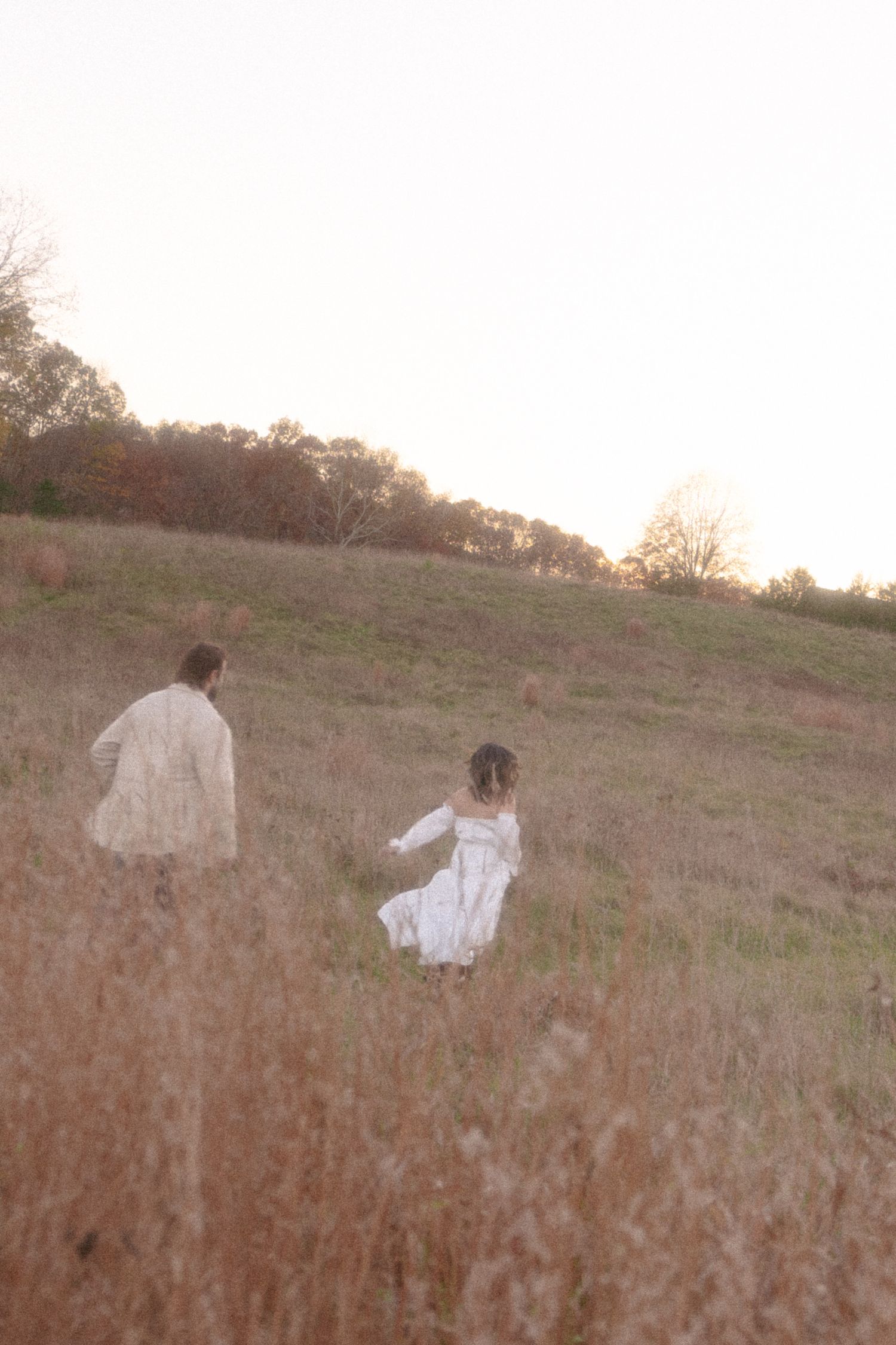 A figure in a flowing white dress runs through a golden field at sunset creating an ethereal silhouette.