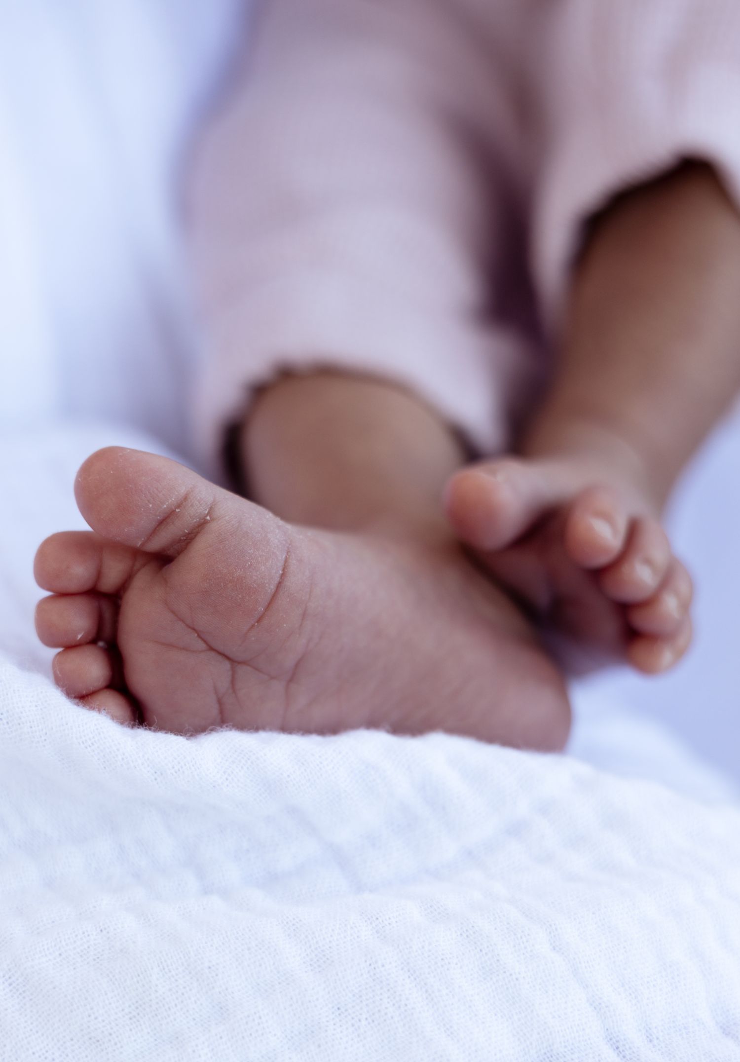 Close-up view of tiny newborn baby feet resting on soft white blanket in gentle natural lighting.