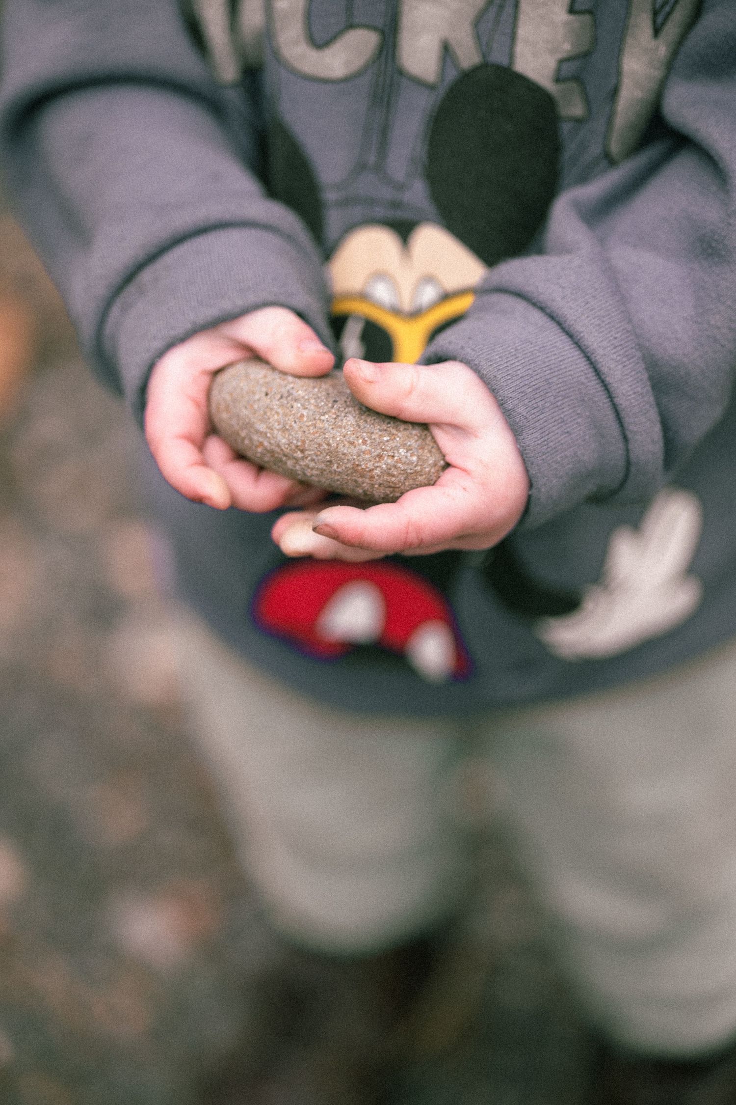 A sequence of hands holding small stones shows a progression of different rocks and pebbles against a dark background.