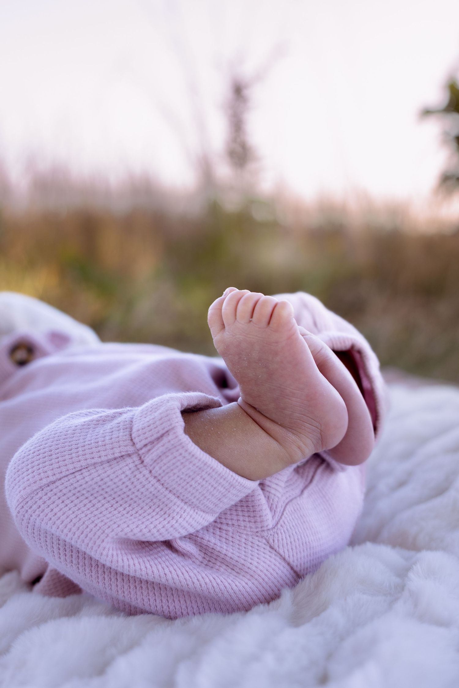 Tiny baby feet wearing soft pink knitted booties resting on white blanket in natural light.